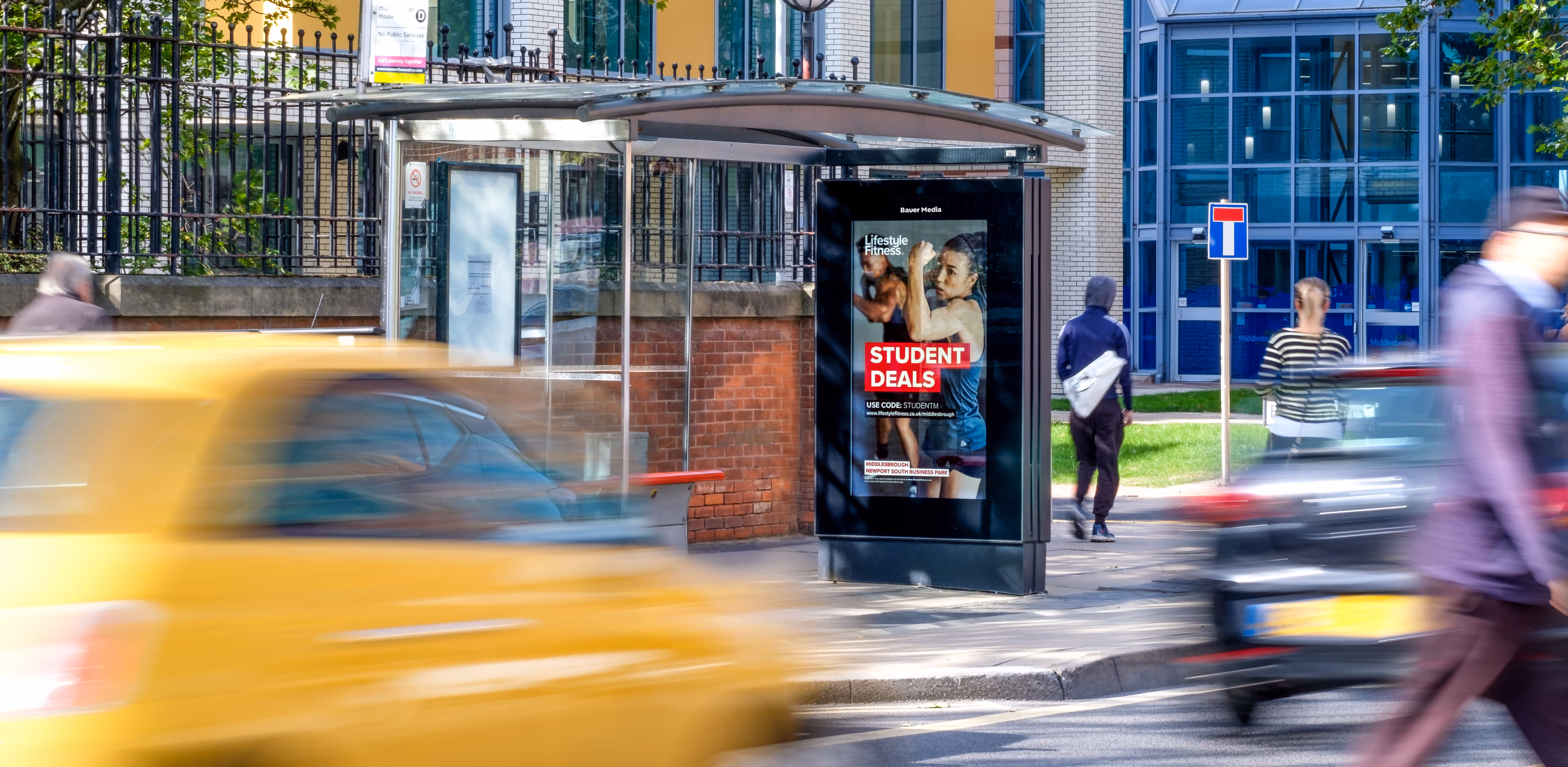 Lifestyle Fitness advertising on a roadside digital screen with people walking by