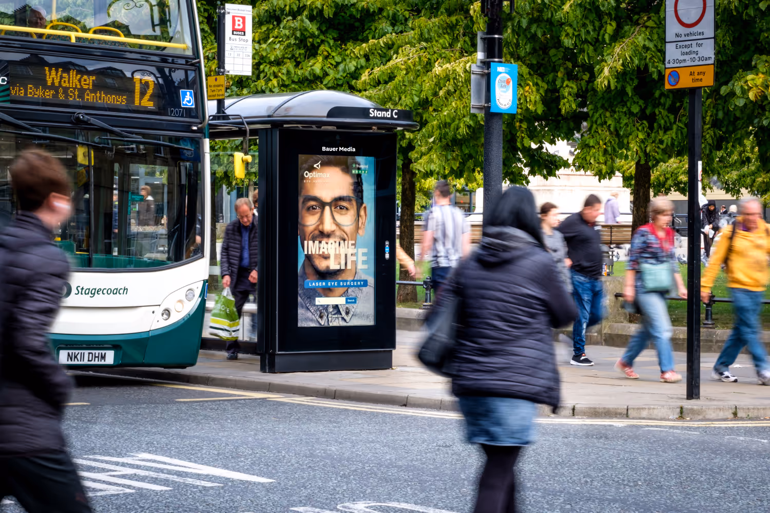 Optimax advertising on a digital screen with a bus stopped at the lights.