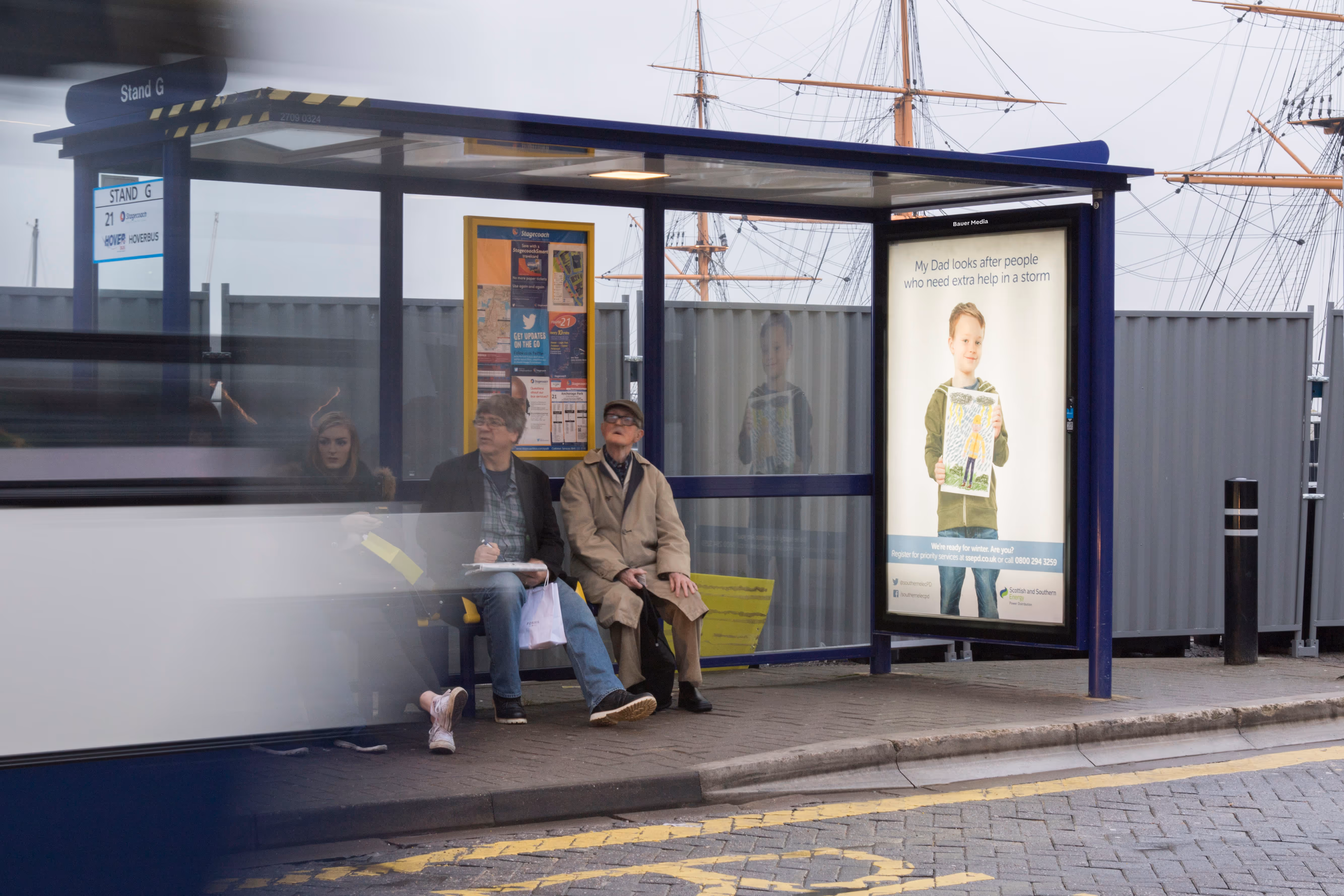 People sat at a local bus stop with a bus stop poster displaying a child