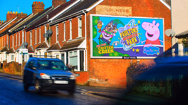 Billboard poster with Peppa Pig displaying next to a car driving by