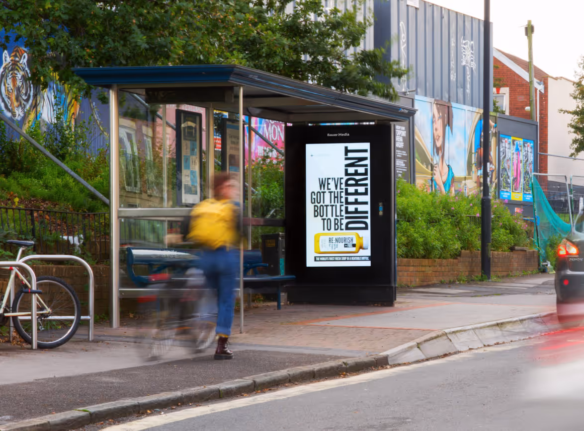 A roadside digital bus stop with a cyclists going by