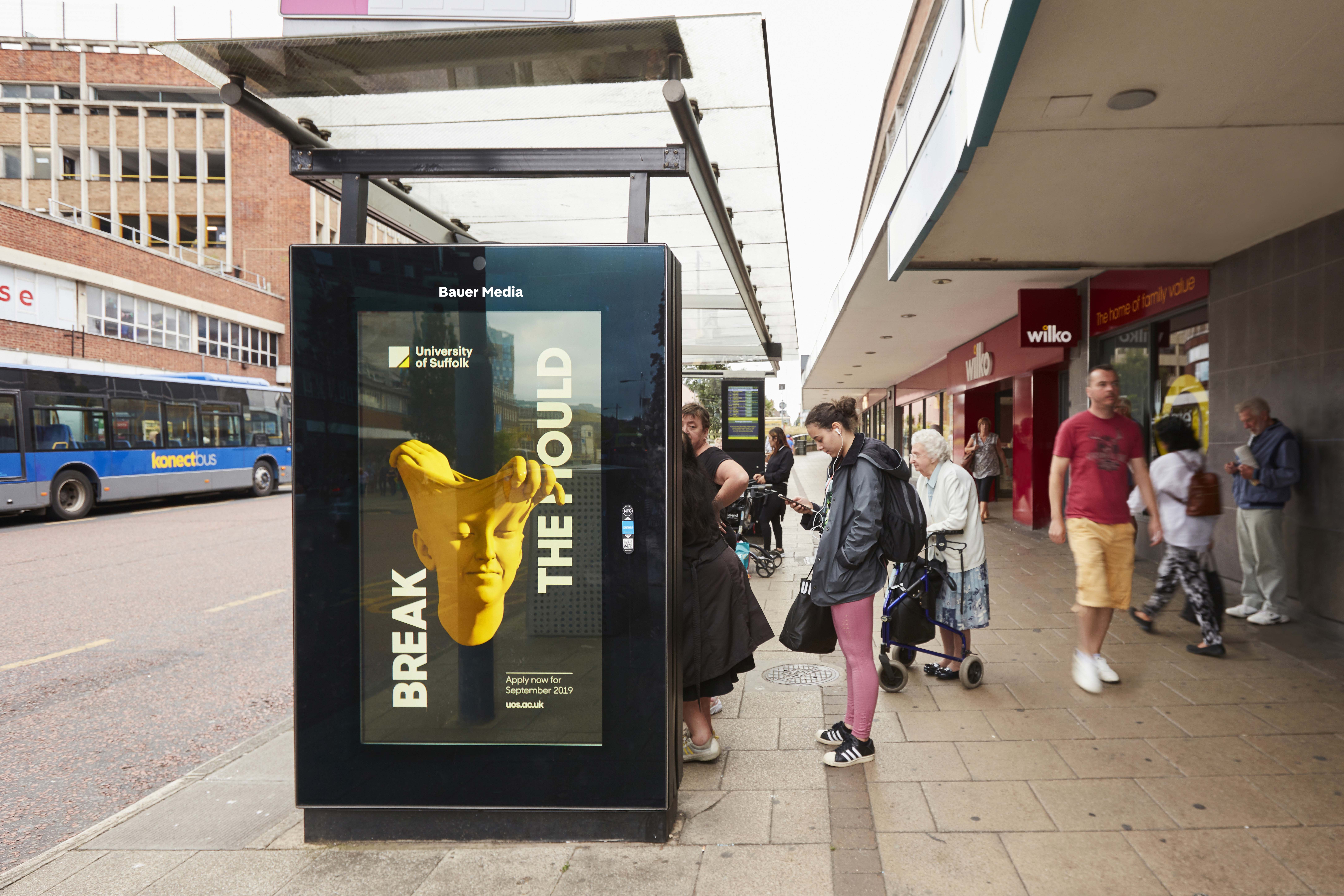 University of Suffolk's "Break the mould" ad as people wait for the bus and walk past