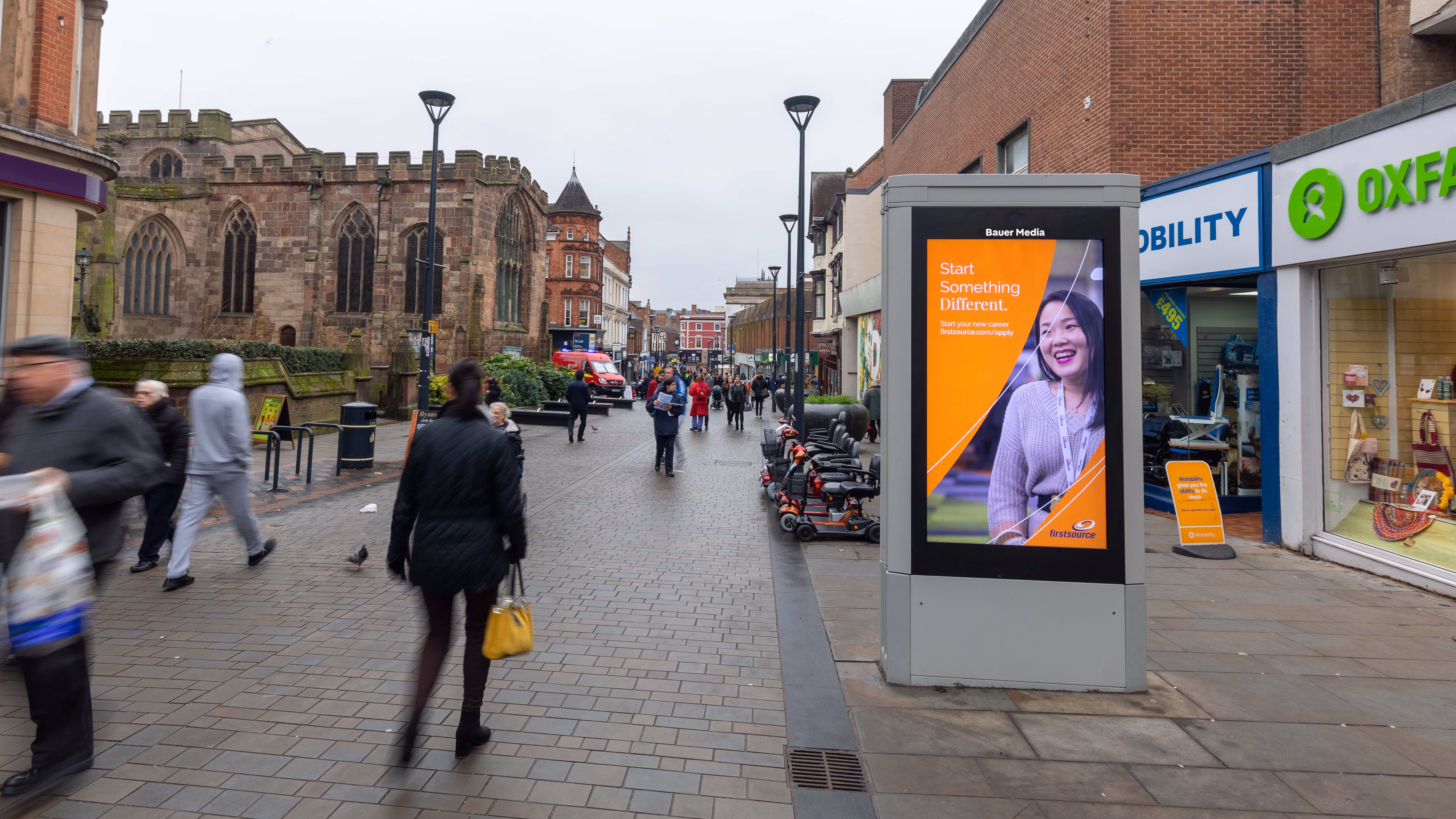 Firstsource's "Start something different" orange ad located on a busy high street
