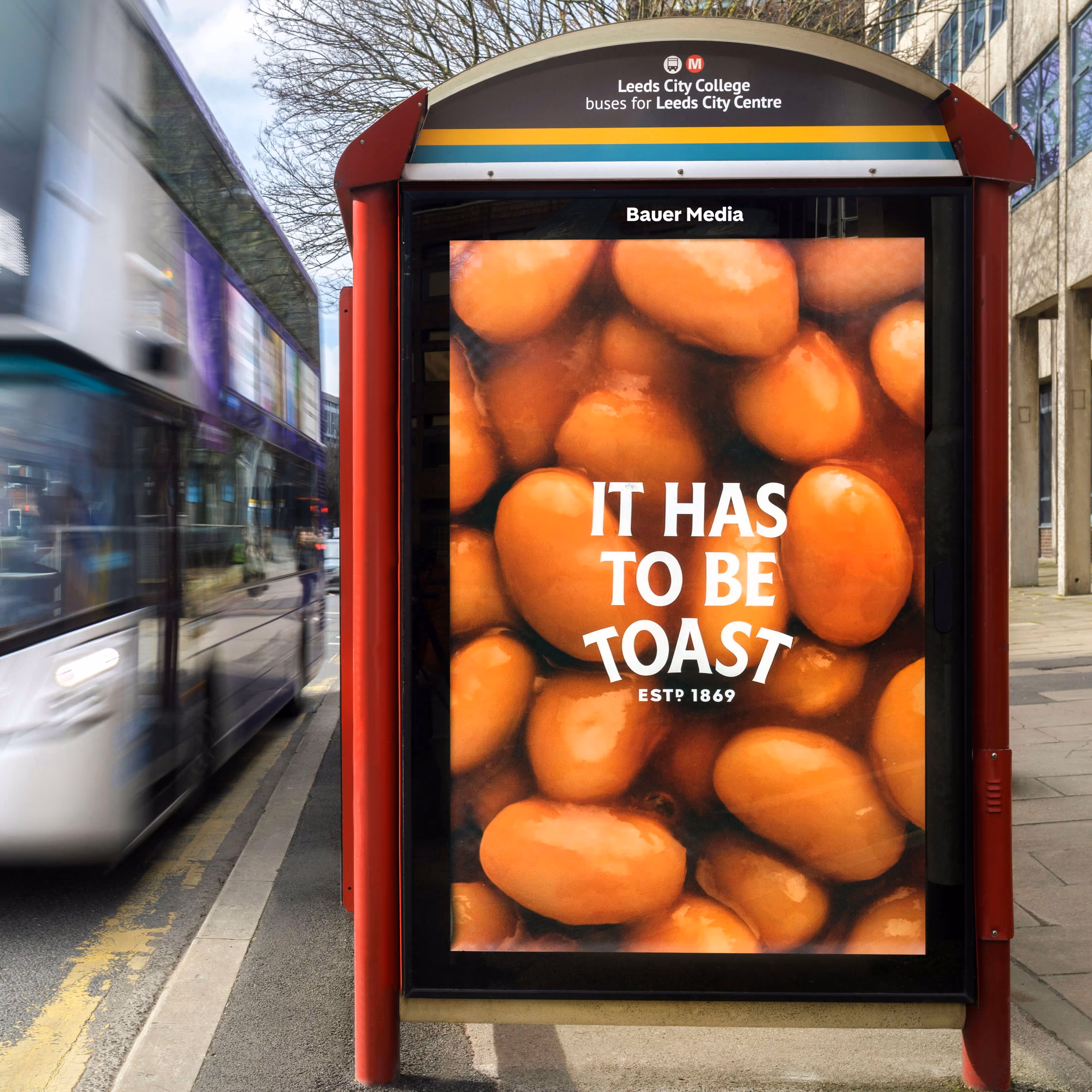 Bauer Media Outdoor digital advertising screen at a bus stop displays a Heinz baked beans ad with the message “It Has to Be Toast,” as a bus passes by