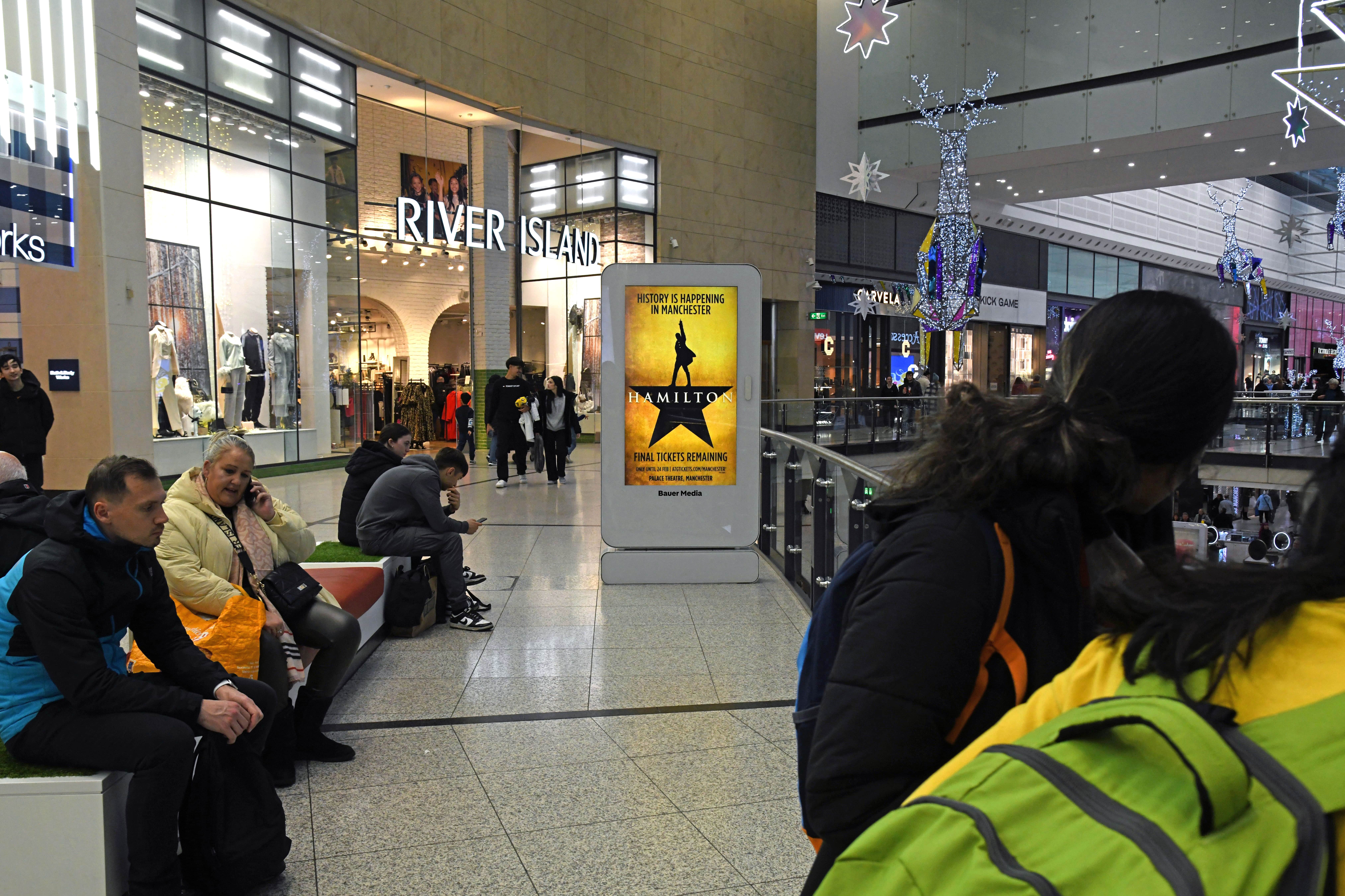 Digital advertisement inside a shopping centre with shoppers walking past