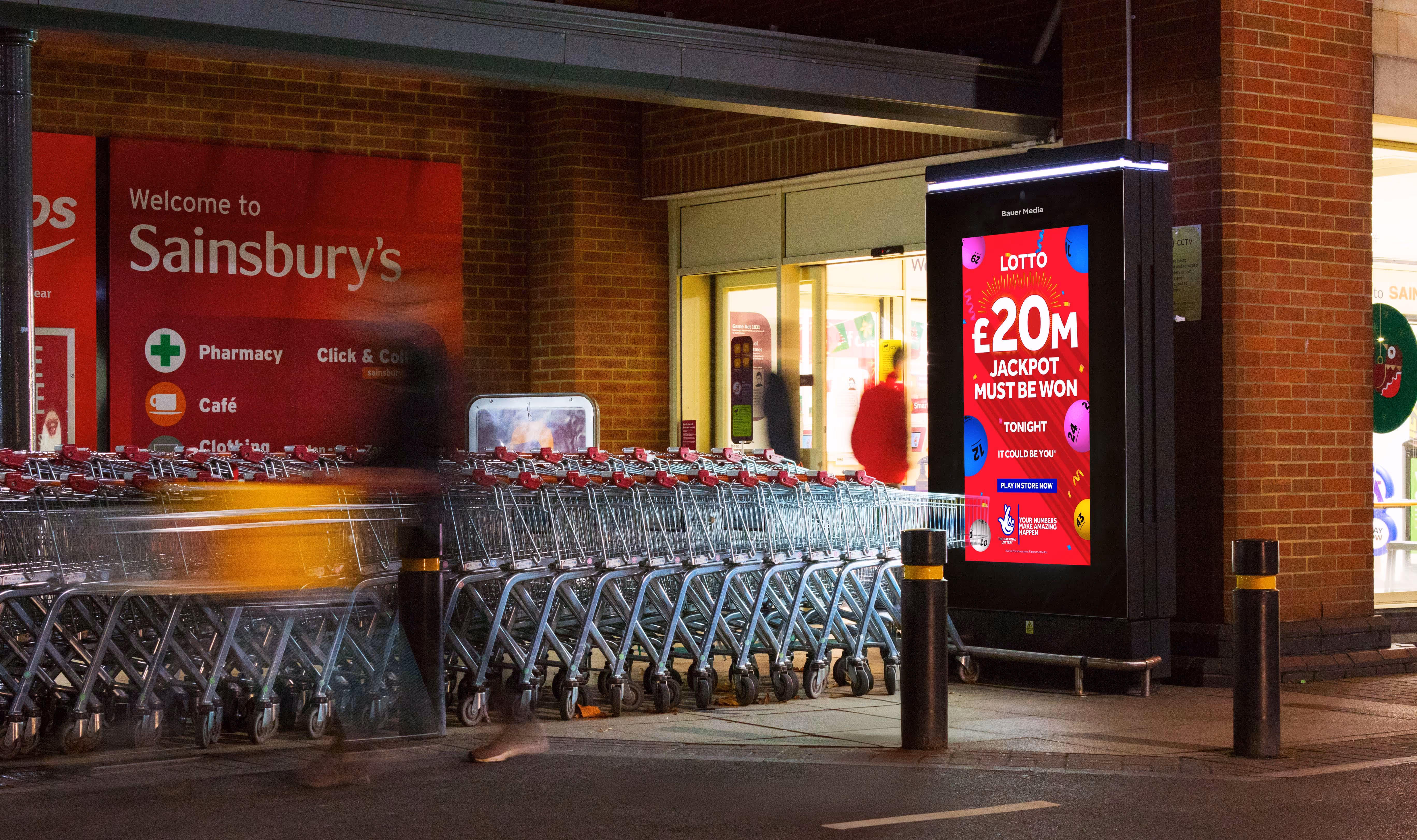 Digital advertisement outside of a Sainsbury's entrance with shoppers walking by