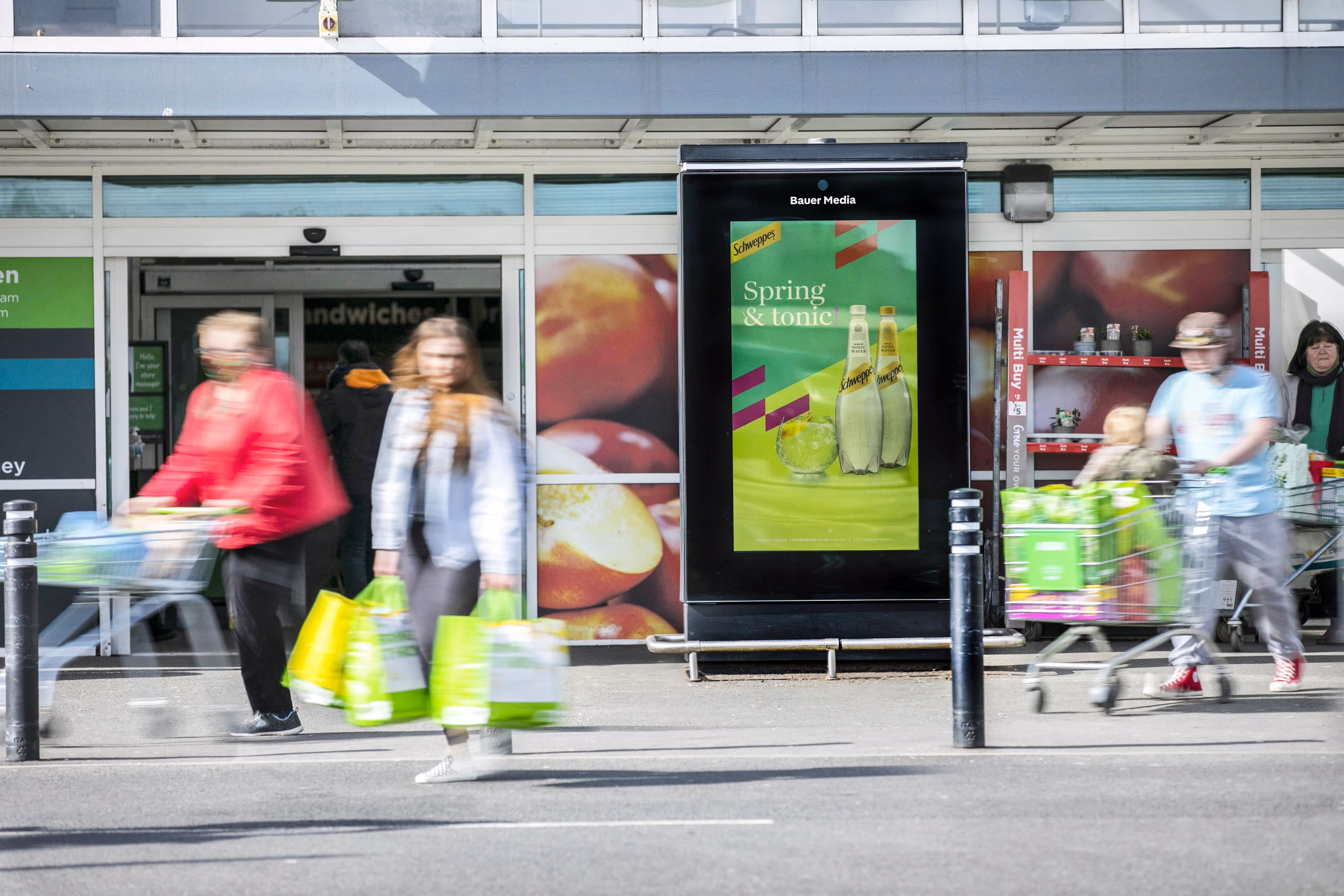 Shoppers walking in front of an Asda during an Schweppes advertisement on Asda Live