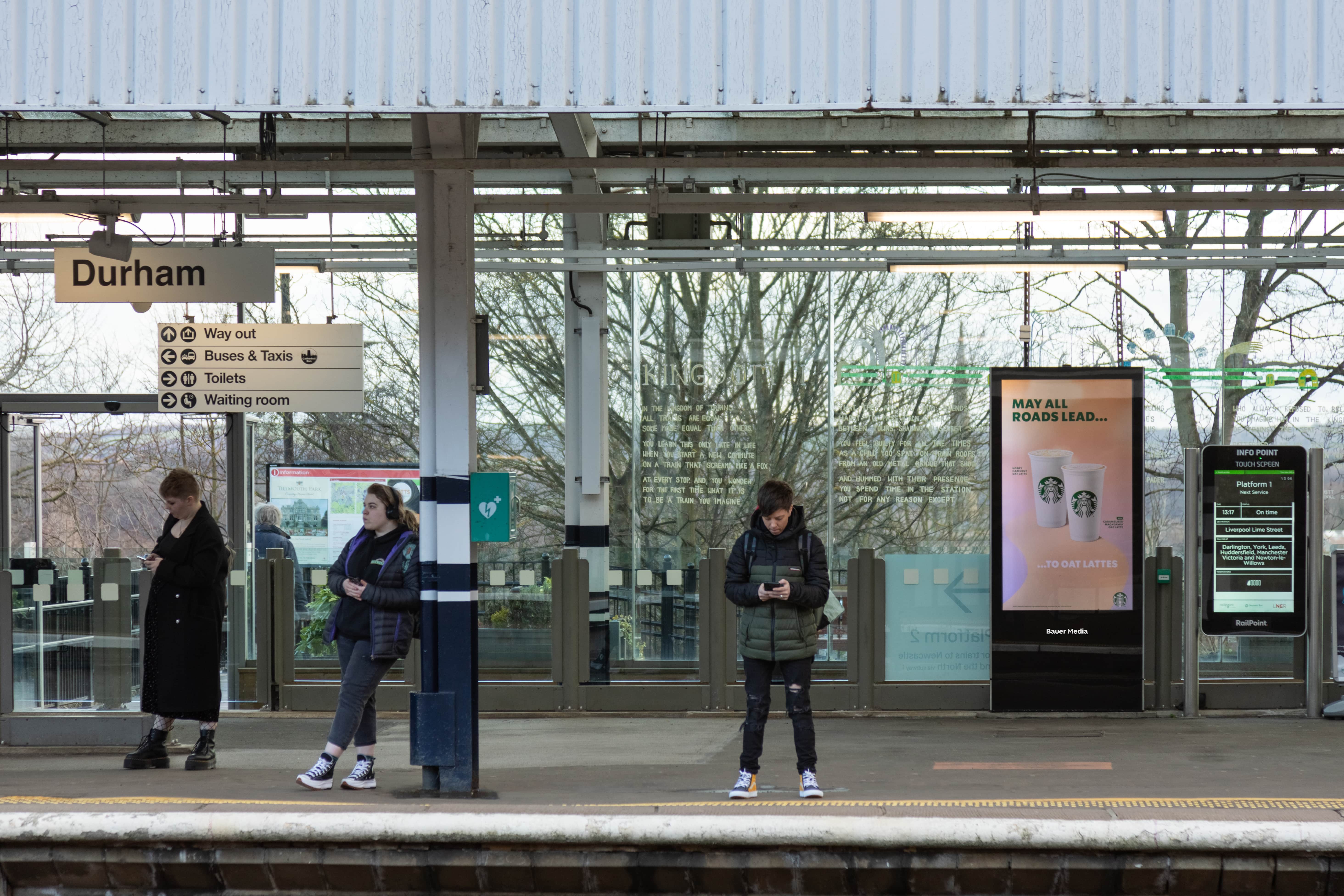 Digital advertisement on the station platform with commuters waiting for their train