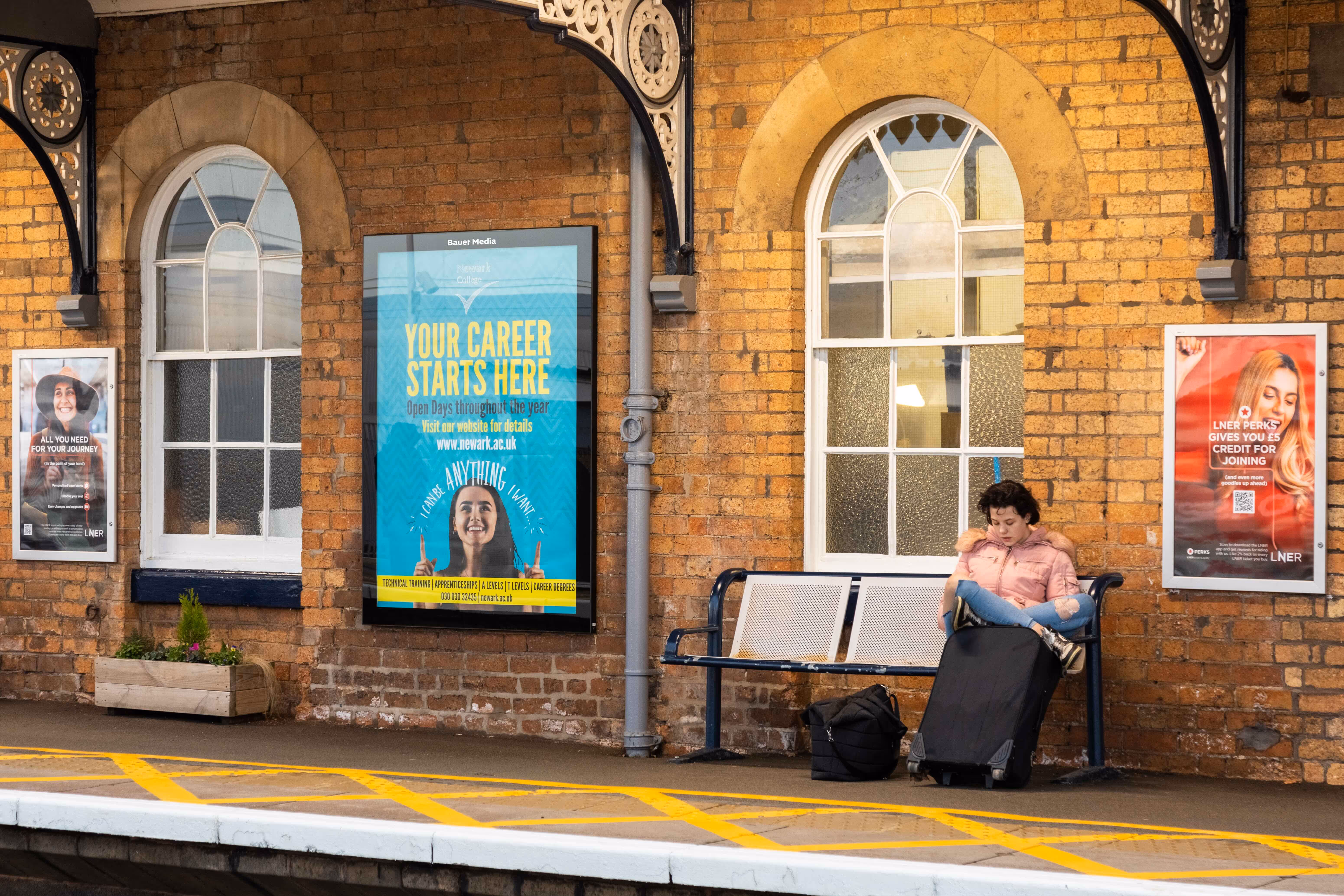 Rail platform showing with billboard showing ad for Newarc university