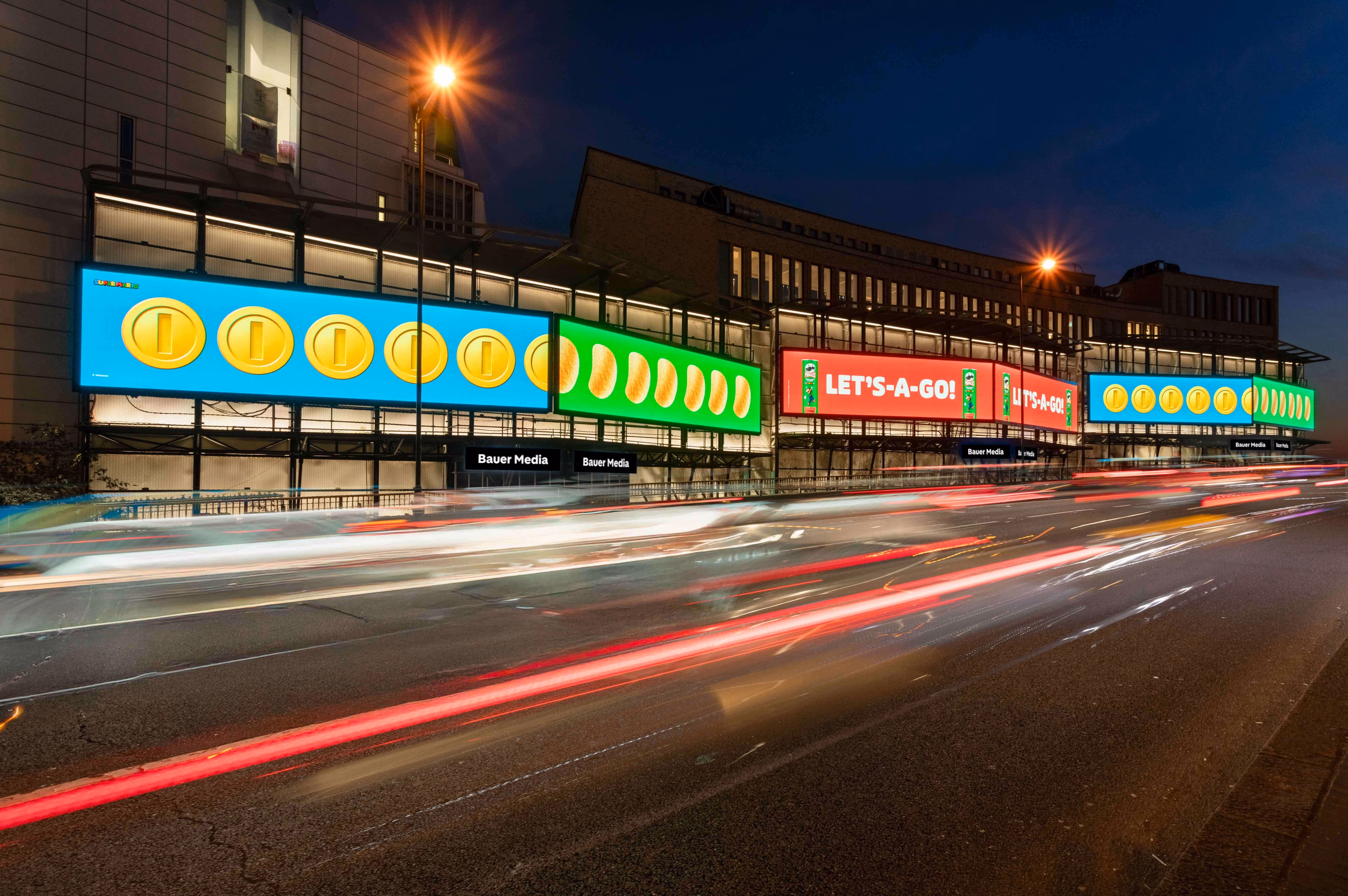 Bauer Media Outdoor digital billboard on cromwell Road displays a vibrant Nintendo Super Mario campaign with coins and the phrase “LET’S-A-GO!”, as traffic blurs past below.