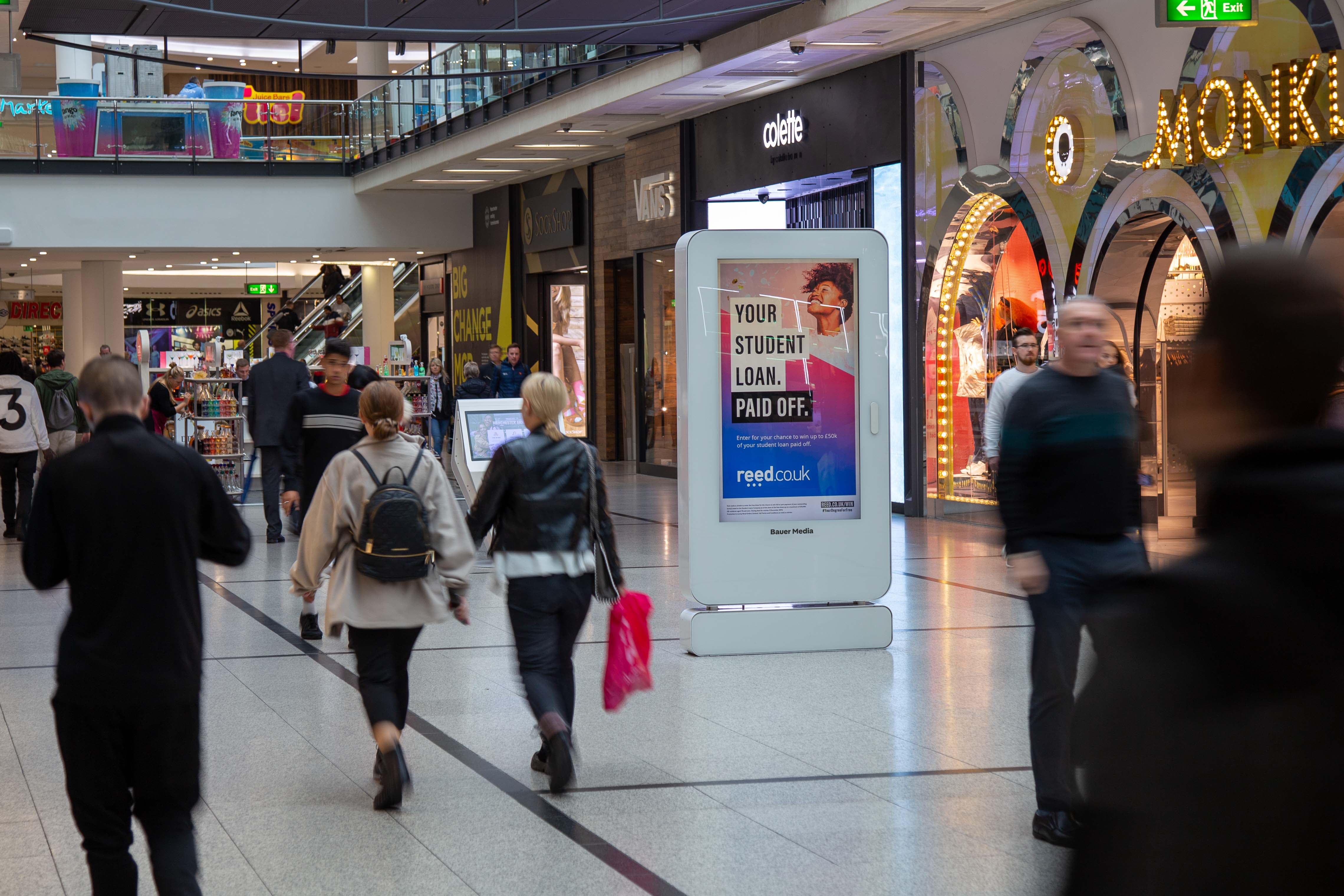 Reed Recruitment advertising on a digital shopping centre screen with shoppers walking past