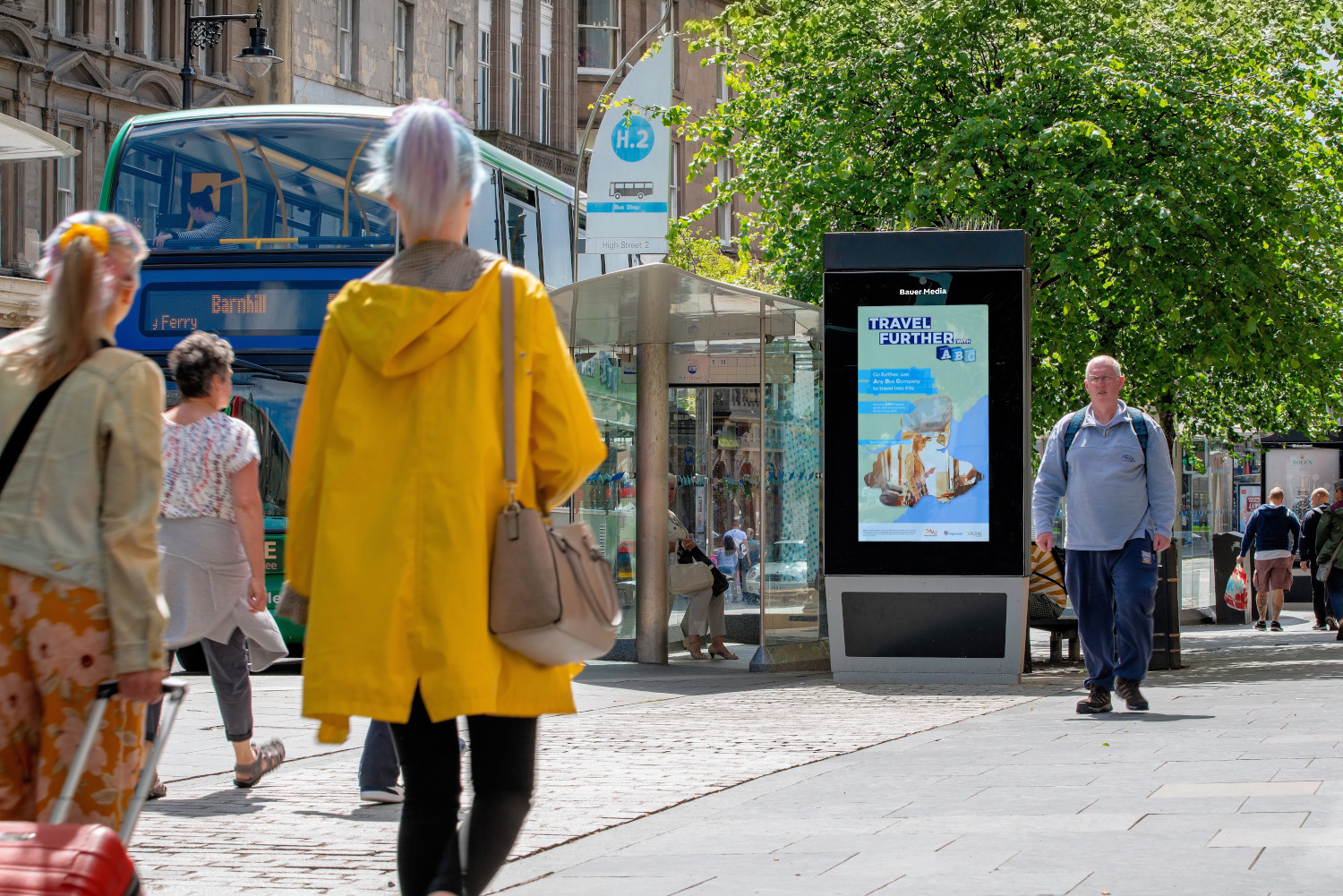 A travel ad campaign displaying on an Adshel Live screen with people walking by
