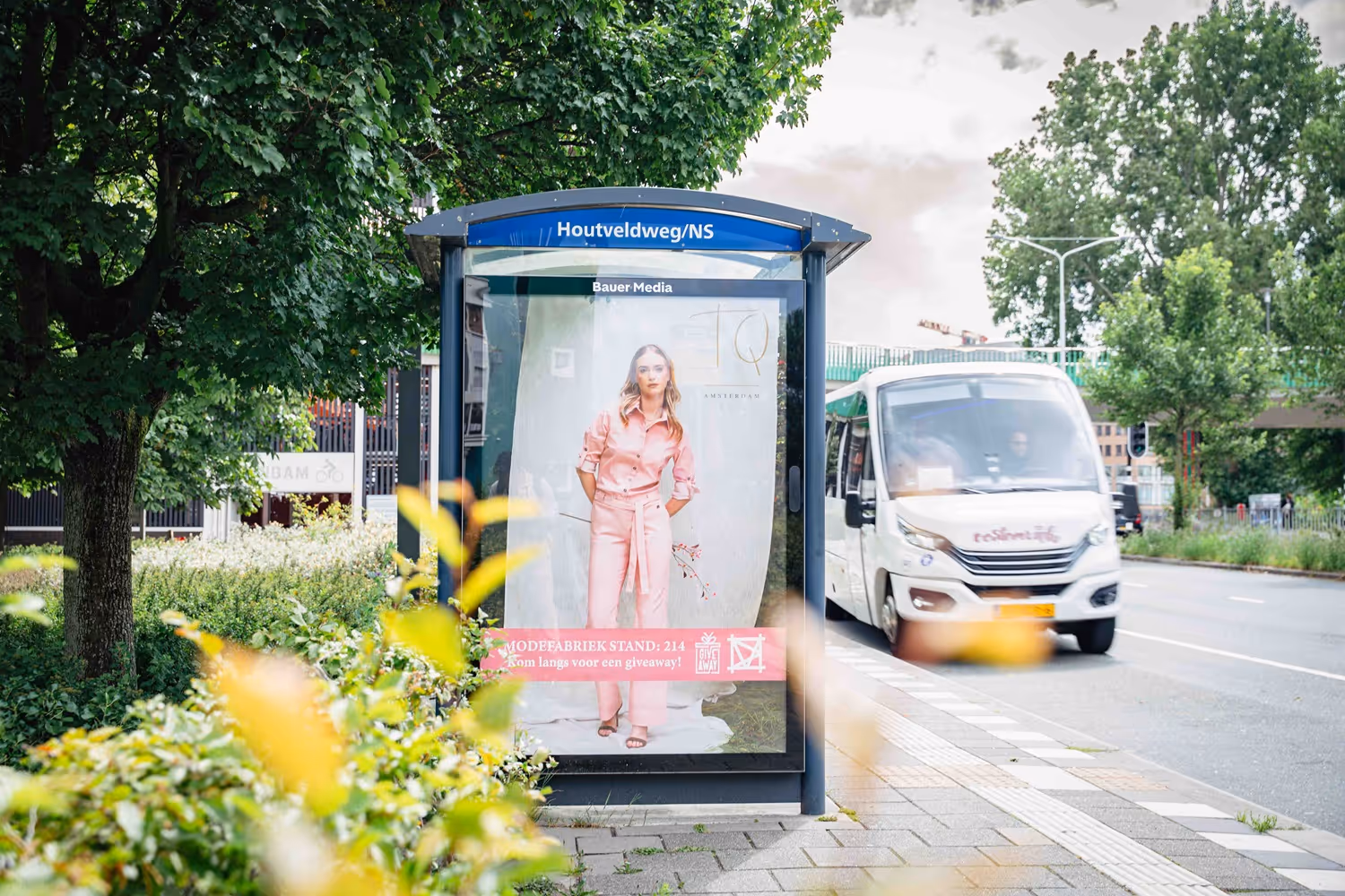 Bushalte langs weg met bus die voorbij rijdt. 