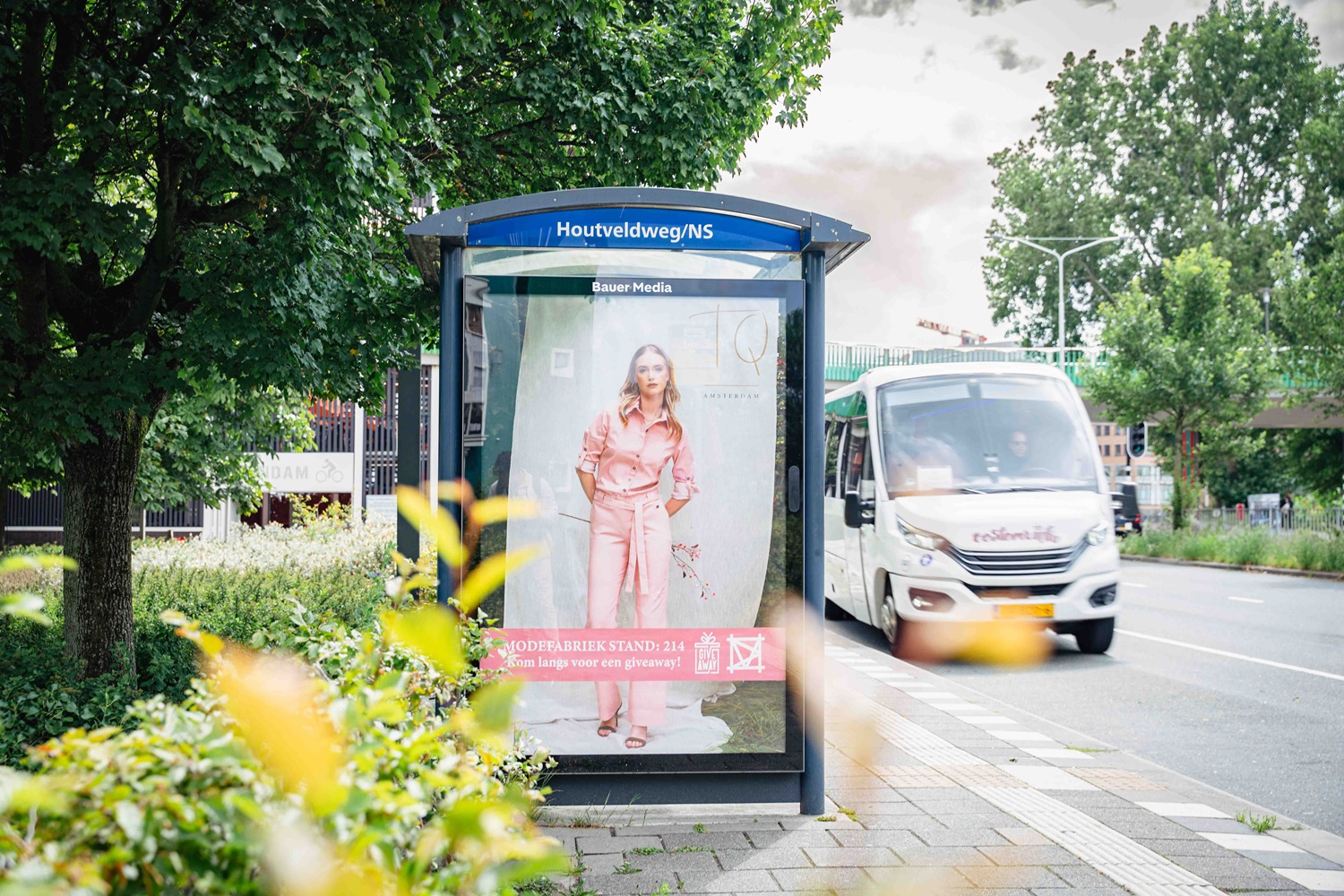 Bushalte langs weg met bus die voorbij rijdt.