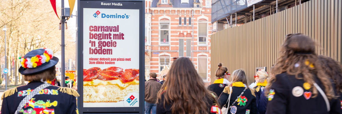 Digitaal scherm met voorbijgangers in carnavalskleding.