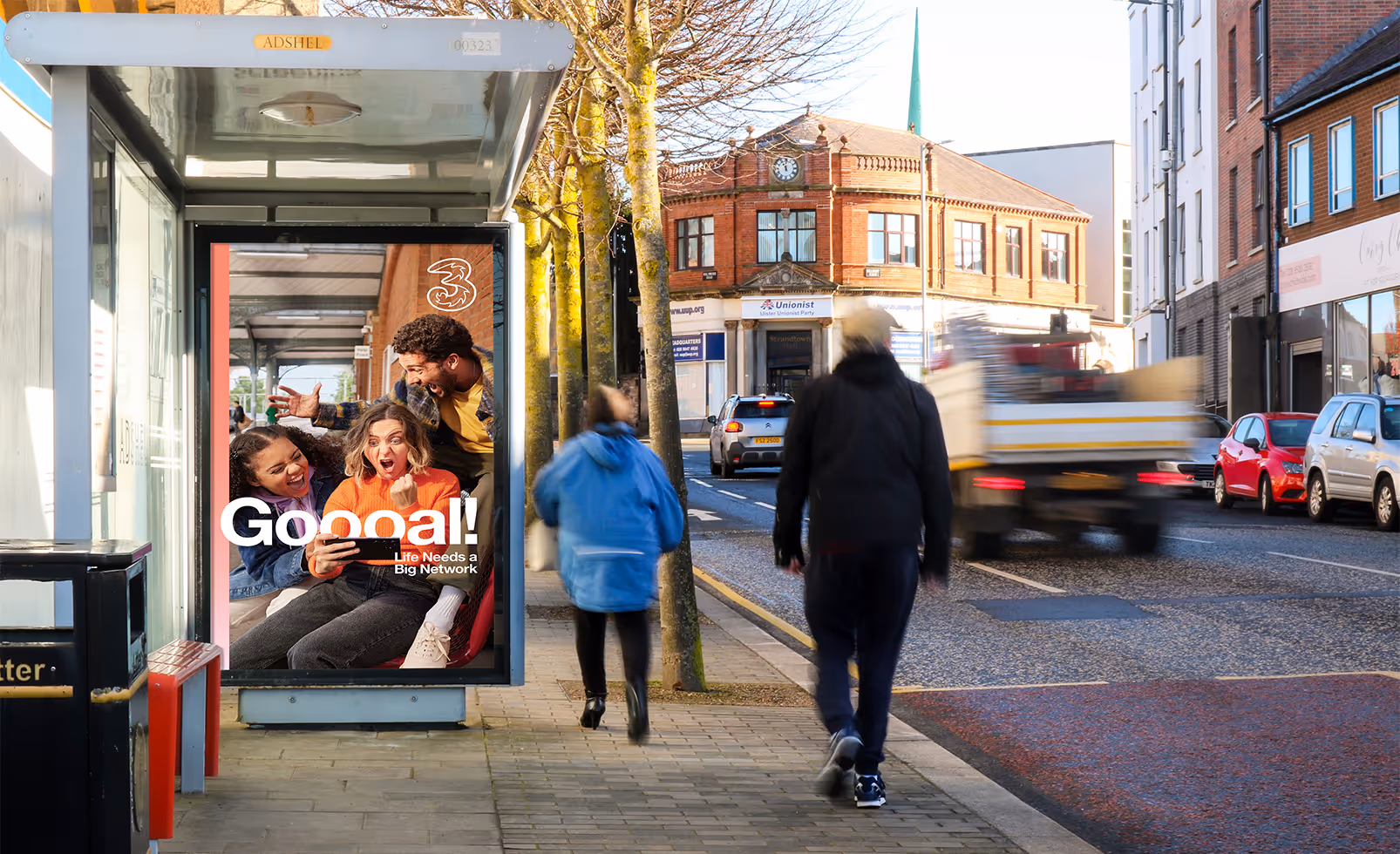 A bus shelter advertisement on a busy London road with people and traffic passing by