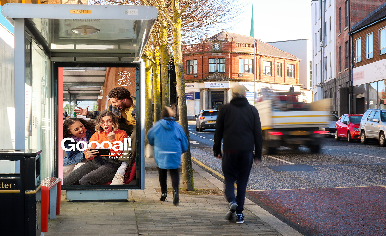 A bus shelter advertisement on a busy London road with people and traffic passing by