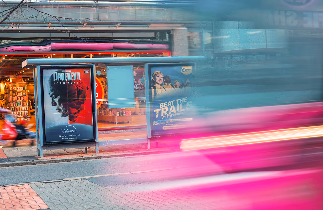 A bus shelter advertisement on a busy street with people walking by and traffic passing