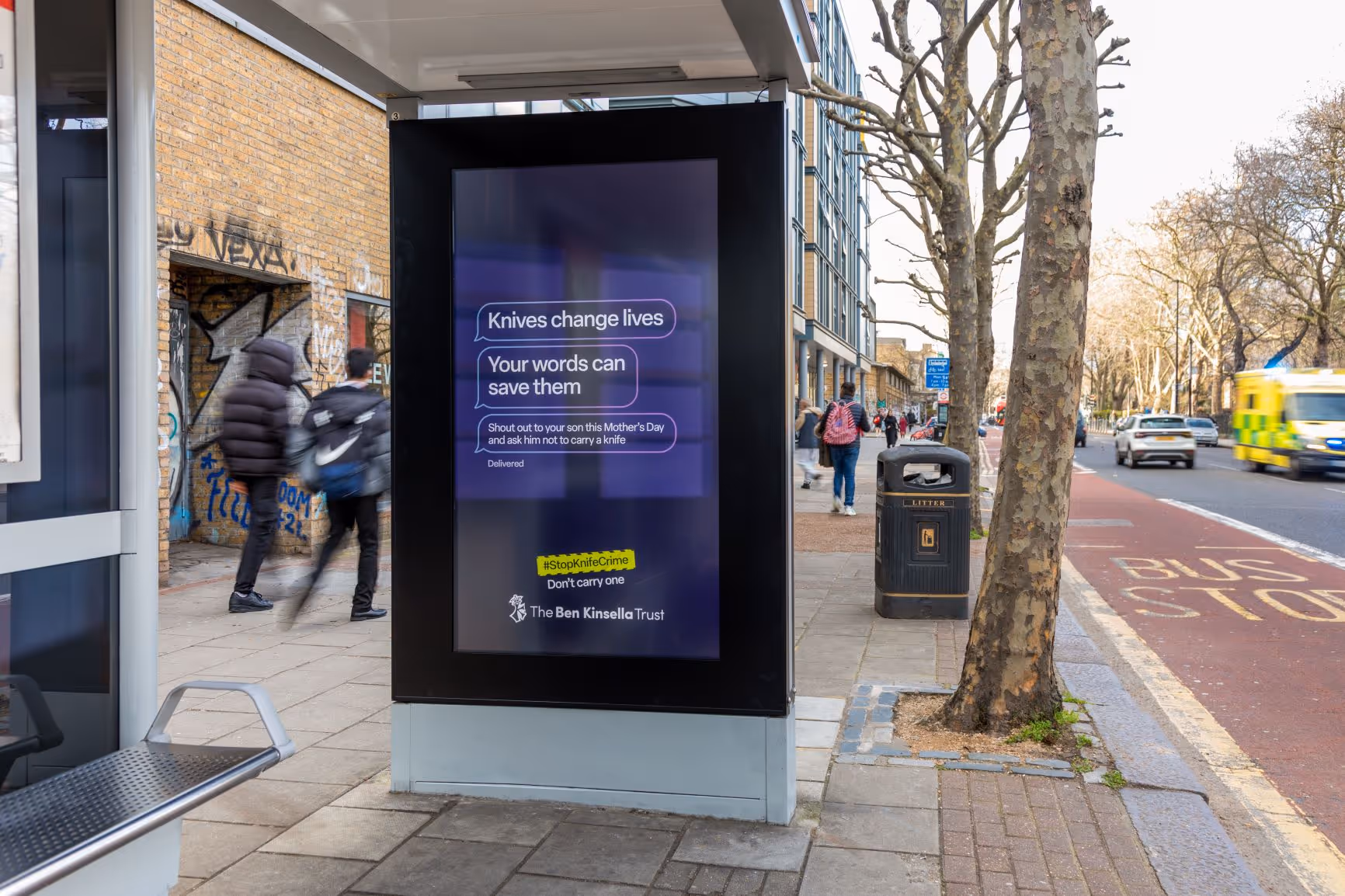 Advertising for the Ben Kinsella Trust featured on a digital screen at a bus stop, during the day, as pedestrians pass by