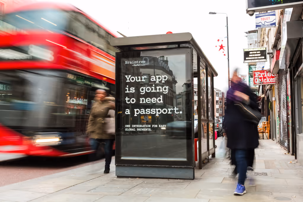 A Braintree advert on the side of a bus shelter, during the day, as pedestrians and buses pass by