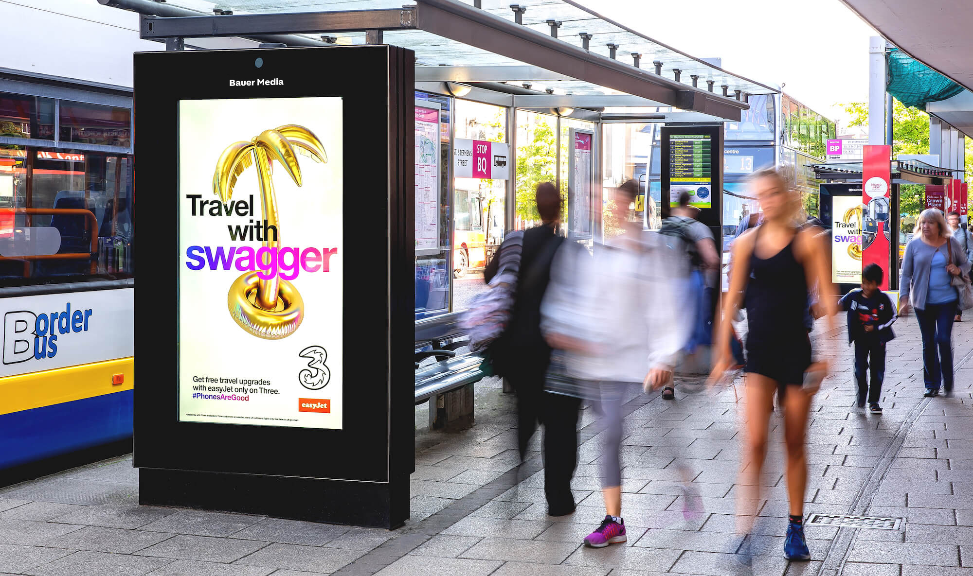 A 3 advert on a digital screen, at a bus stop on a busy sidewalk, during the day, as pedestrians pass by 