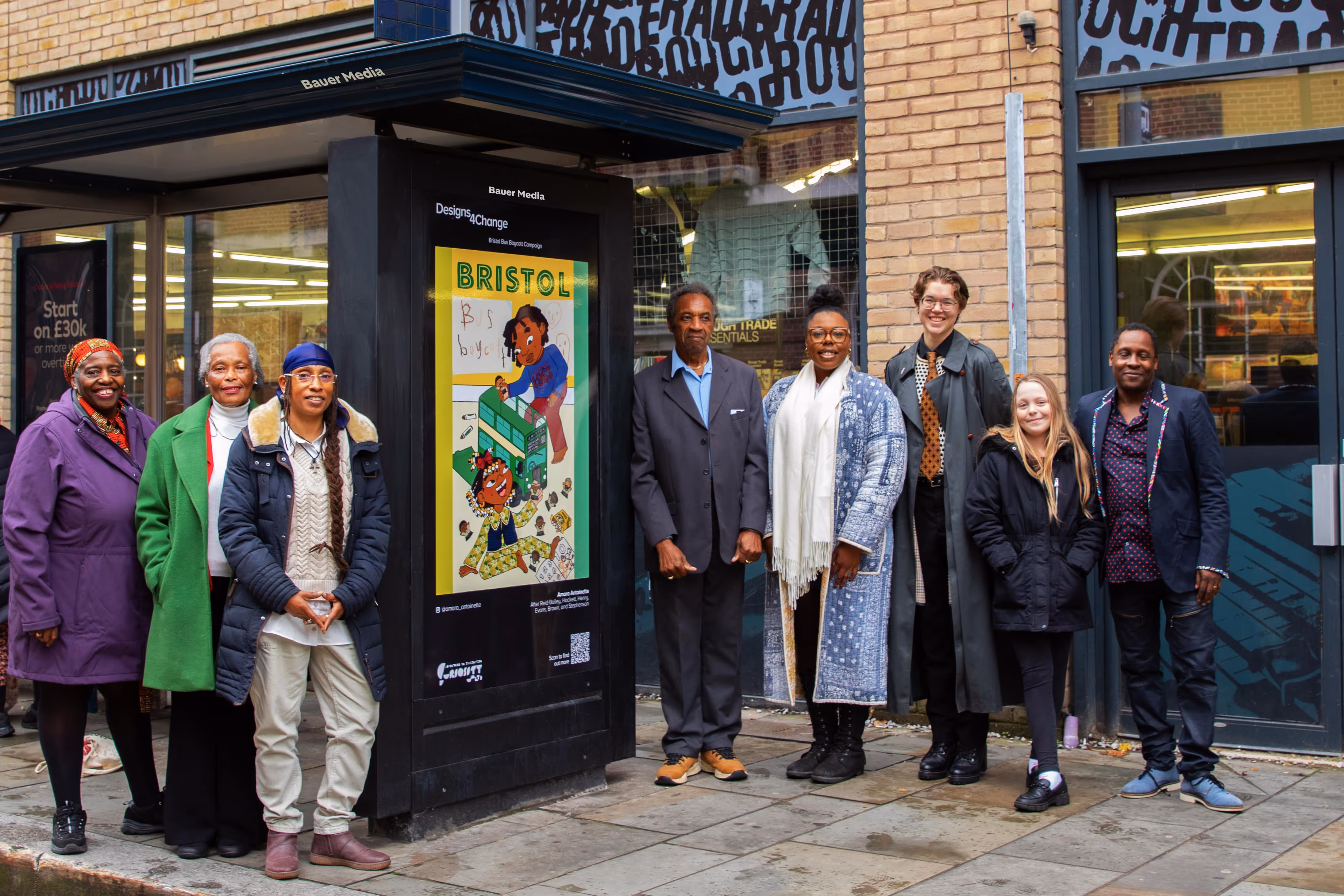 Winners of the Designs4Change competition stand next to a bus stop featuring an advert of one of the winning artworks
