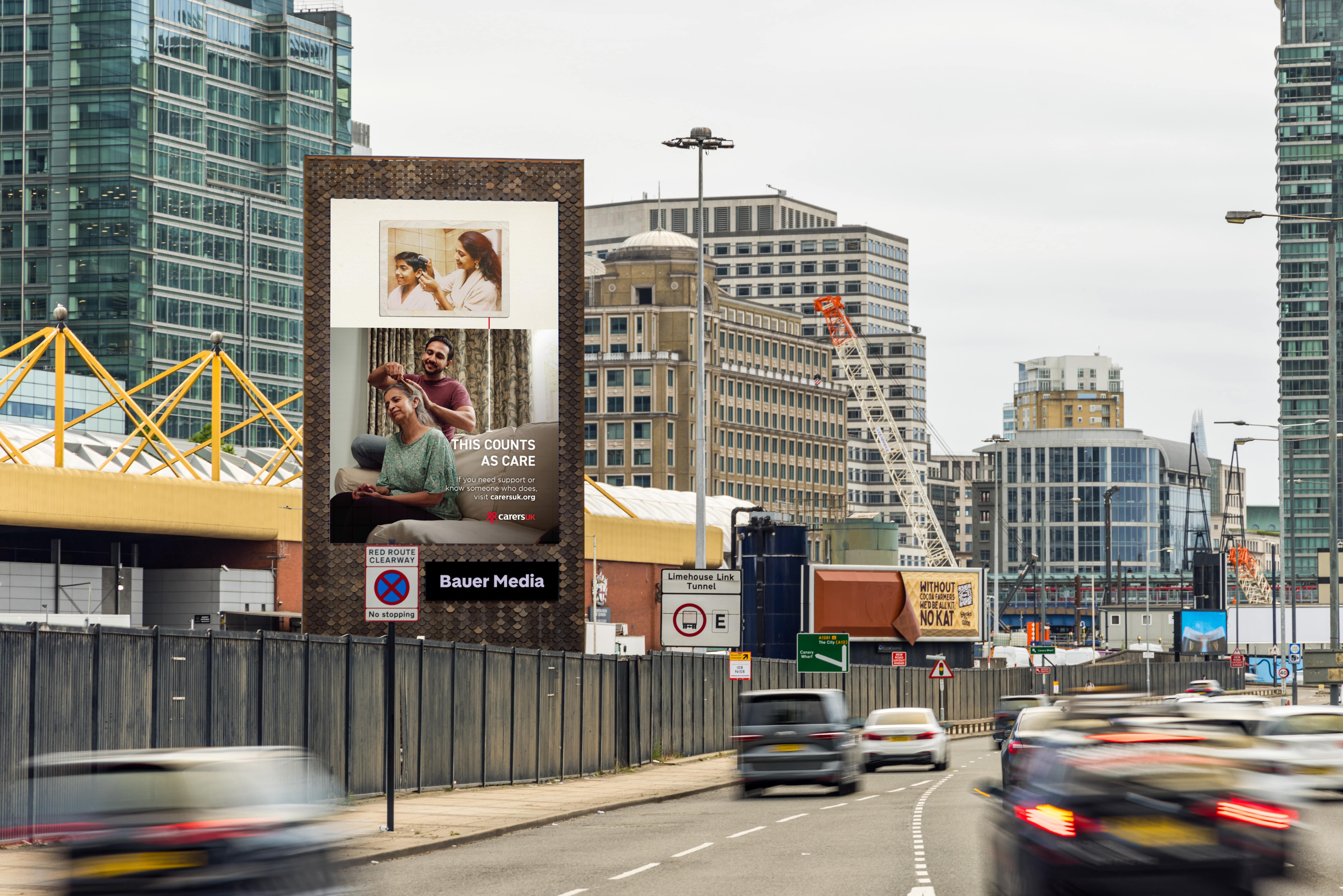 Carers UK 'This Counts as Care' campaign advert on a Storm screen by Billingsgate Market, during the day, as cars drive by
