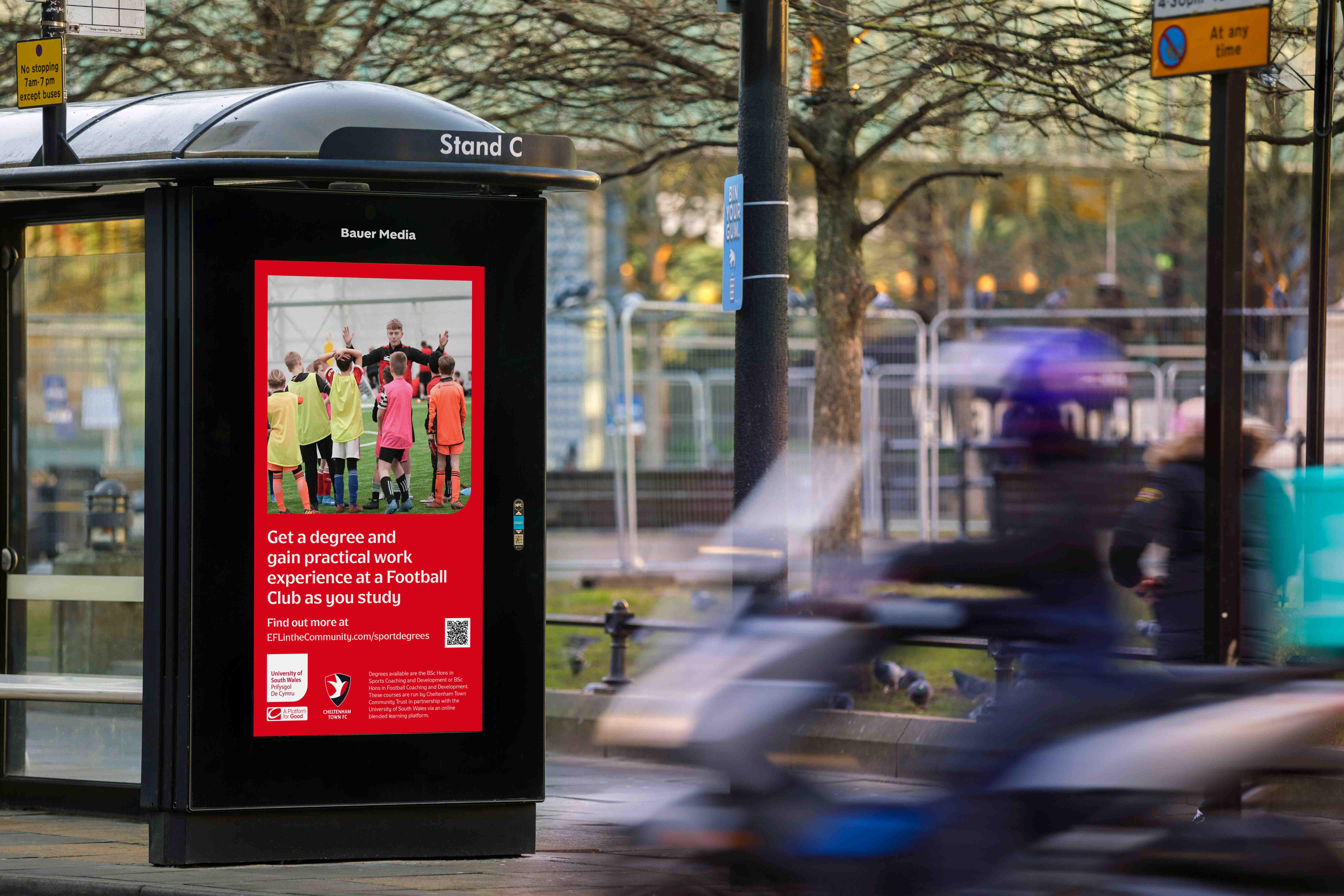EFL advertising featured on a digital screen at a bus shelter, during the day, as vehicles drive by
