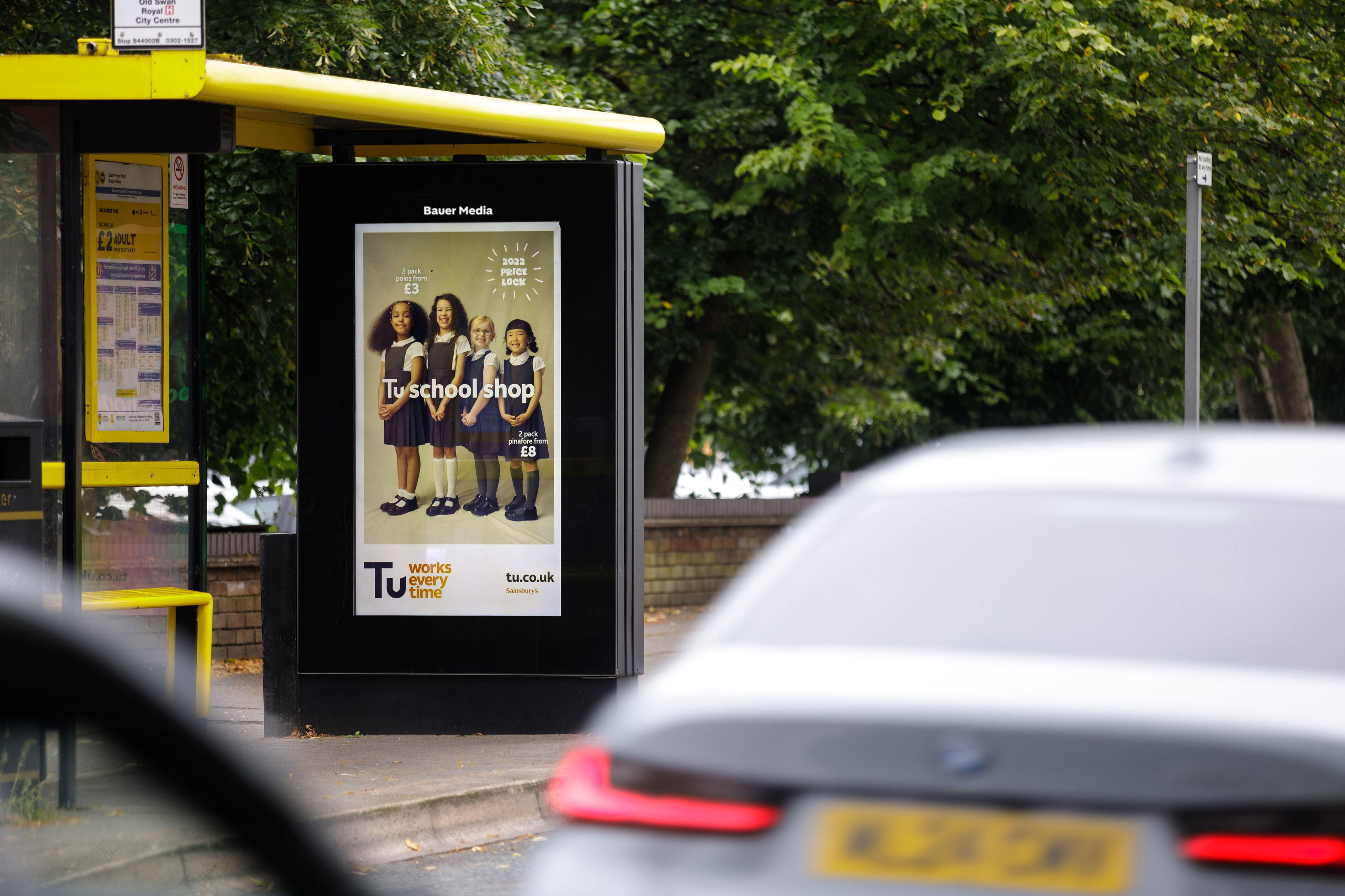 A digital screen at a bus shelter showing an ad for Tu clothing