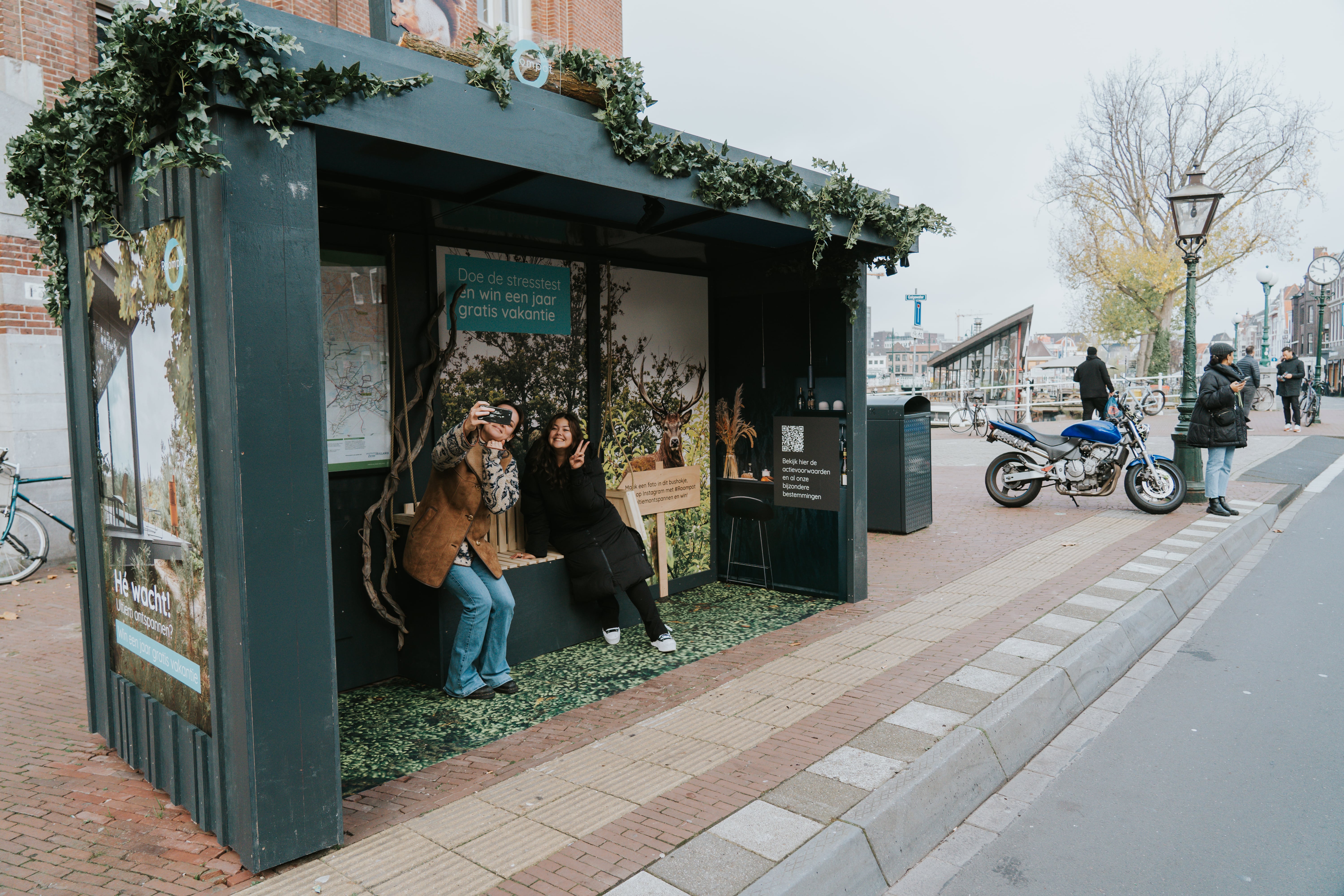 Bushalte met houten bekleding en 2 dames zitten in bushalte en maken een foto