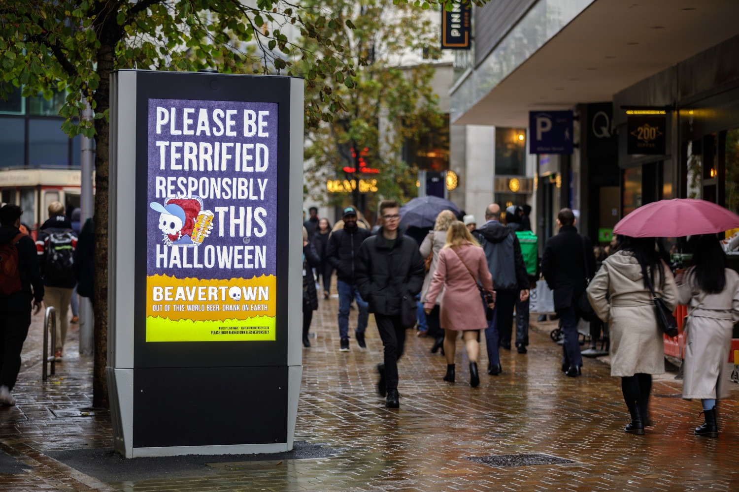 Beavertown Halloween advert on a digital screen outside a store as shoppers walk pass during the day