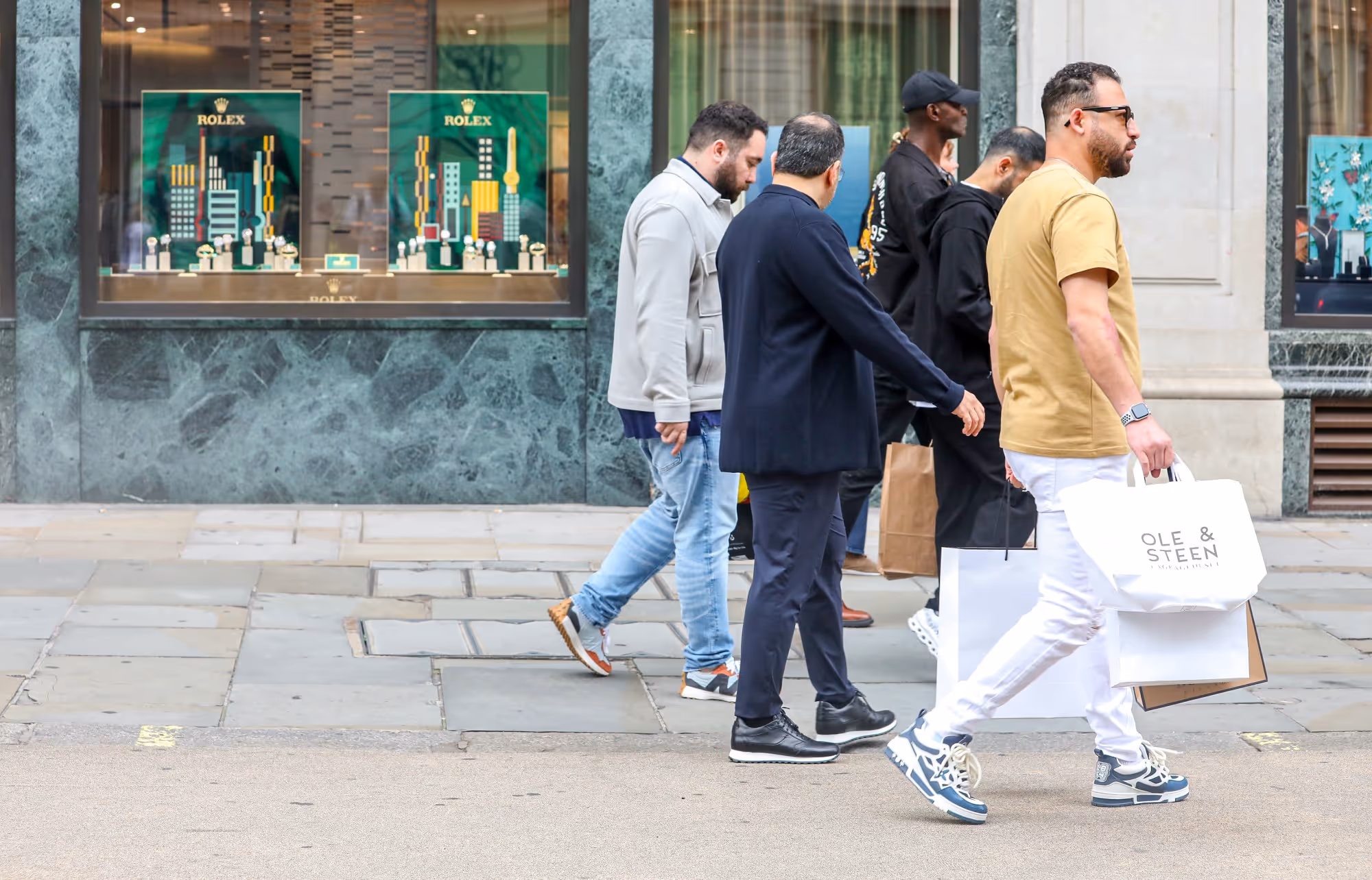 Group of men with shopping bags walking on the pavement
