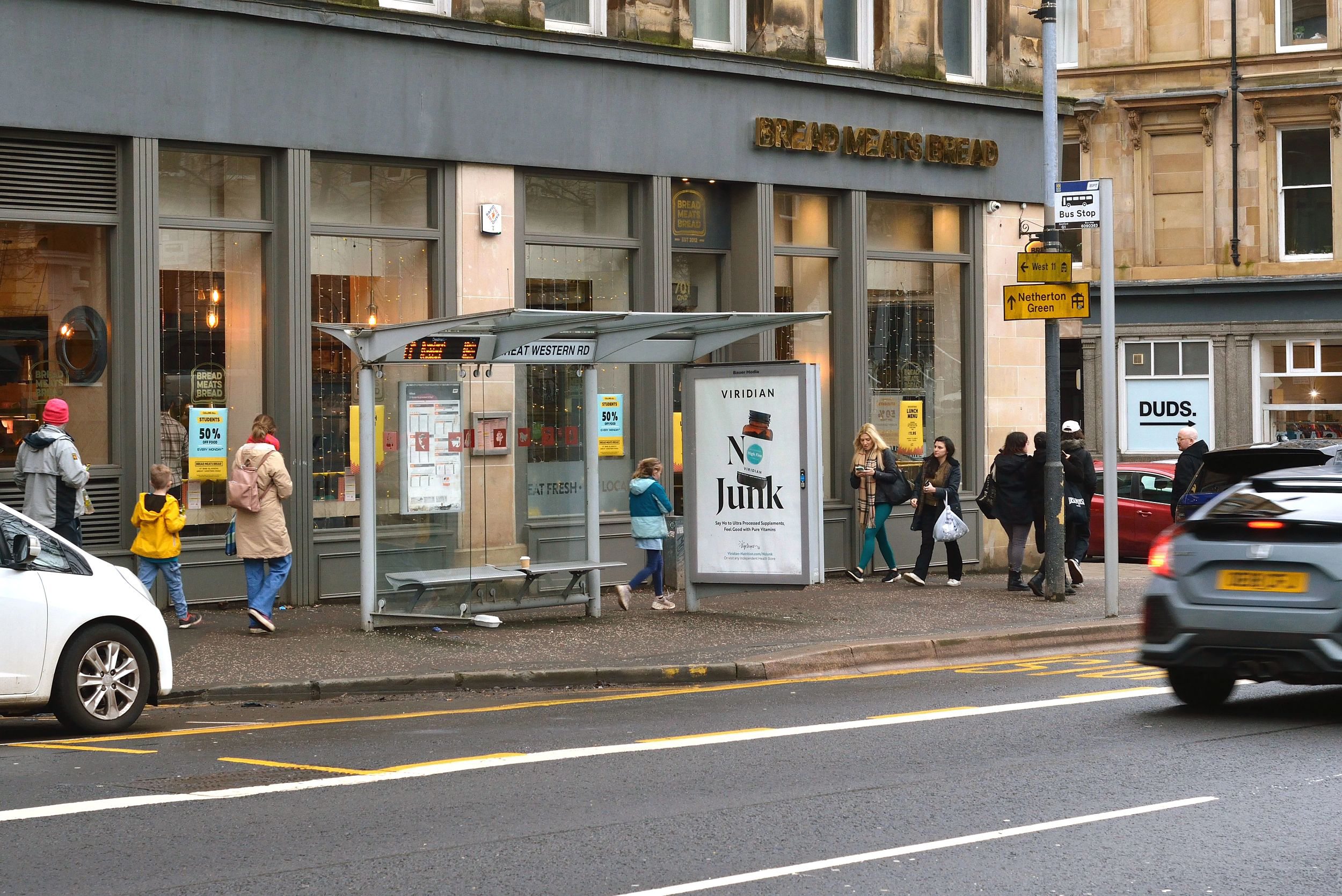 A Viridian ad campaign displaying on a bus stop outside of a bar with people walking past
