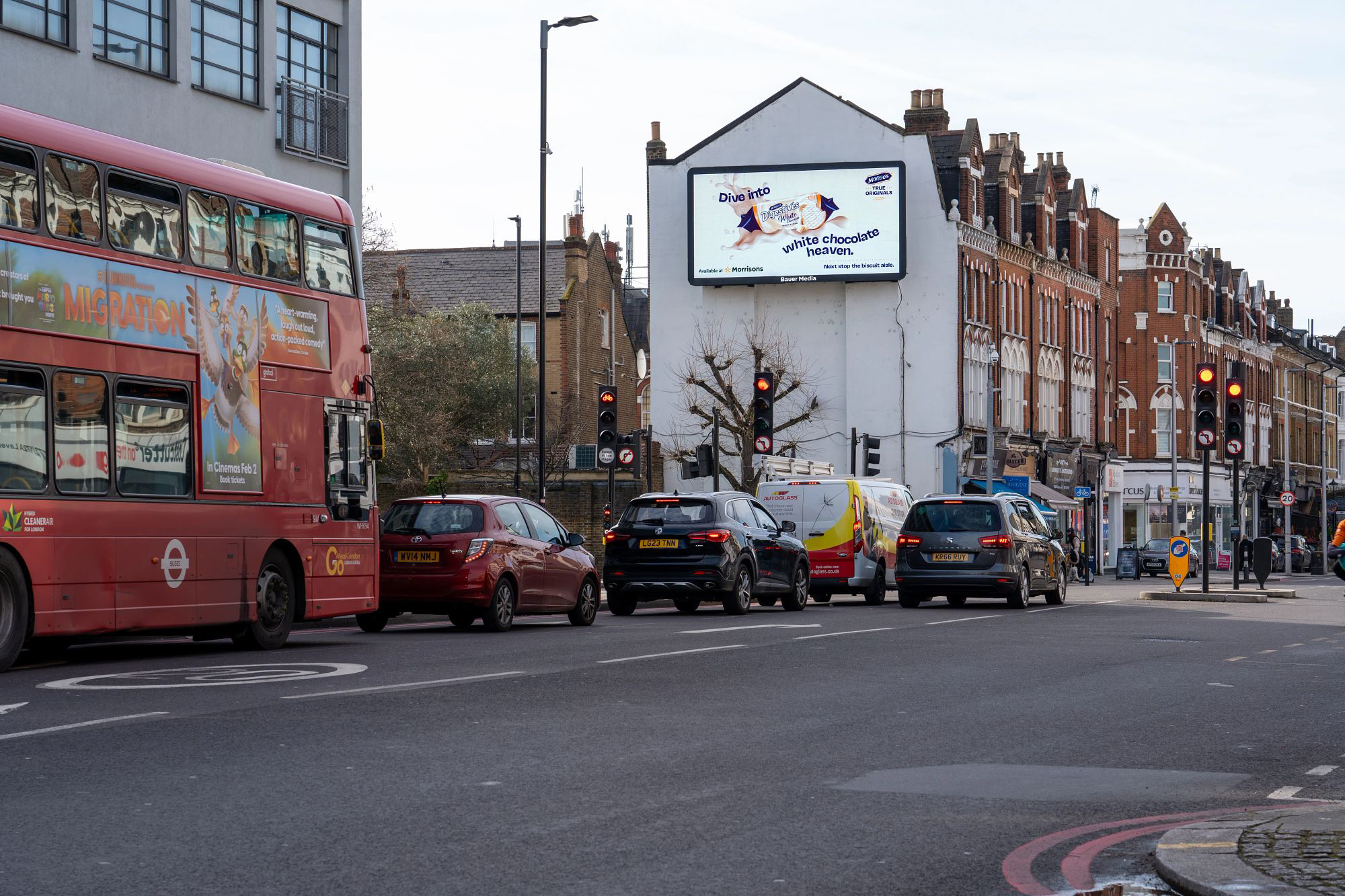Digital billboard on the side of a building with a red bus driving past