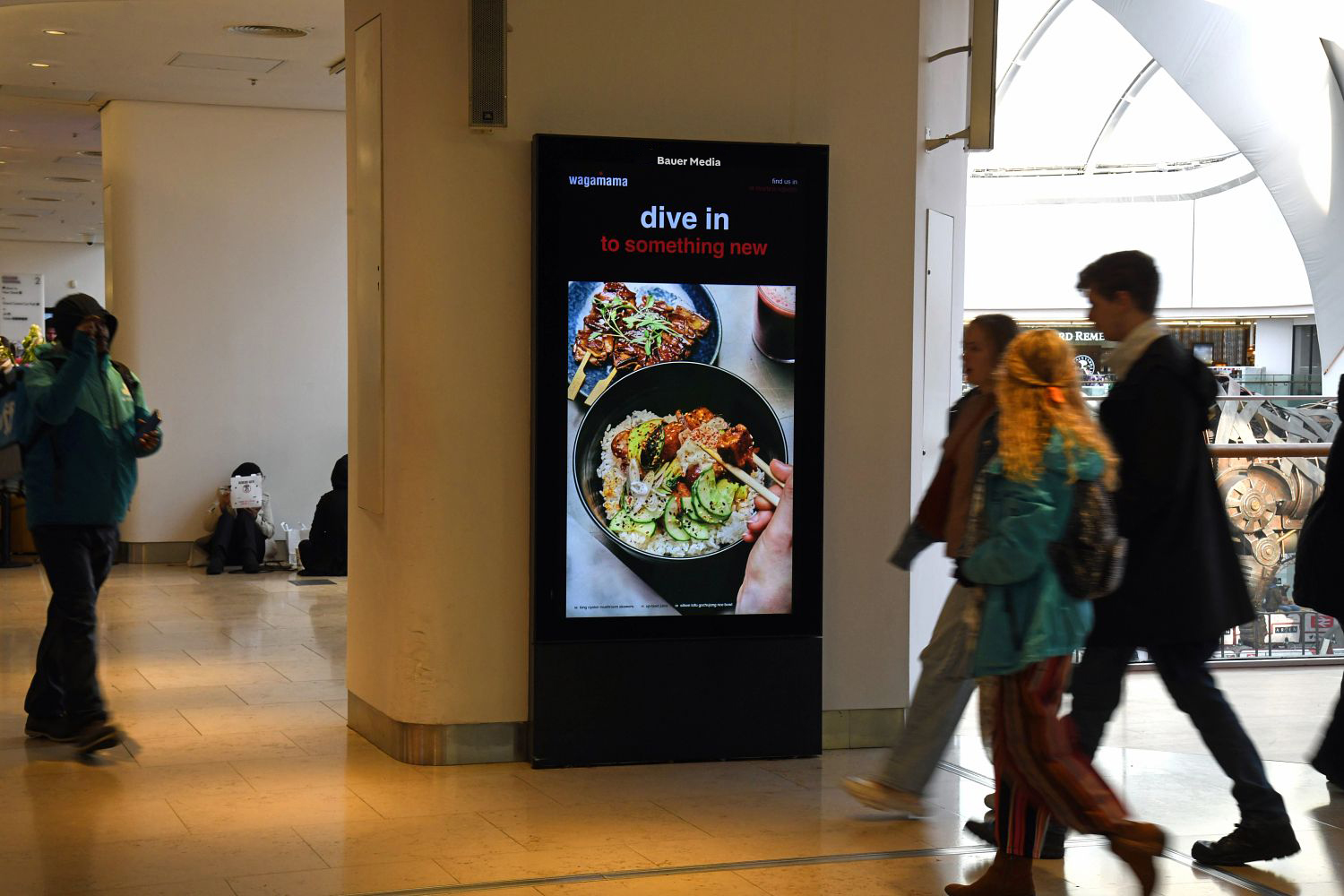 Wagamama advertising inside a shopping centre with shoppers walking past