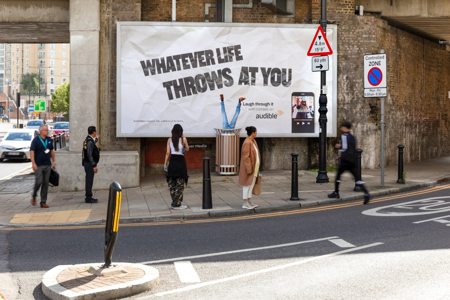 Audible creative billboard campaign featuring a pair of legs hanging upside down in a bin