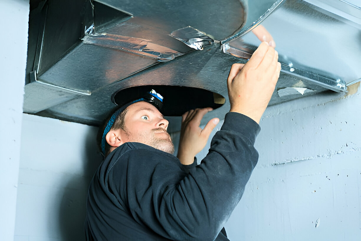 Worker in blue hat inspecting or repairing overhead ductwork