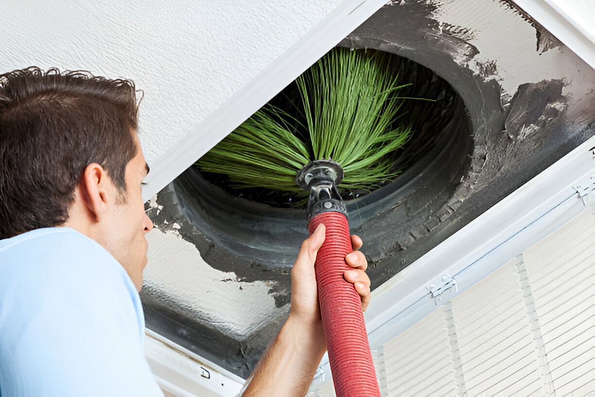 Person cleaning air vent with green brush attachment inside ceiling