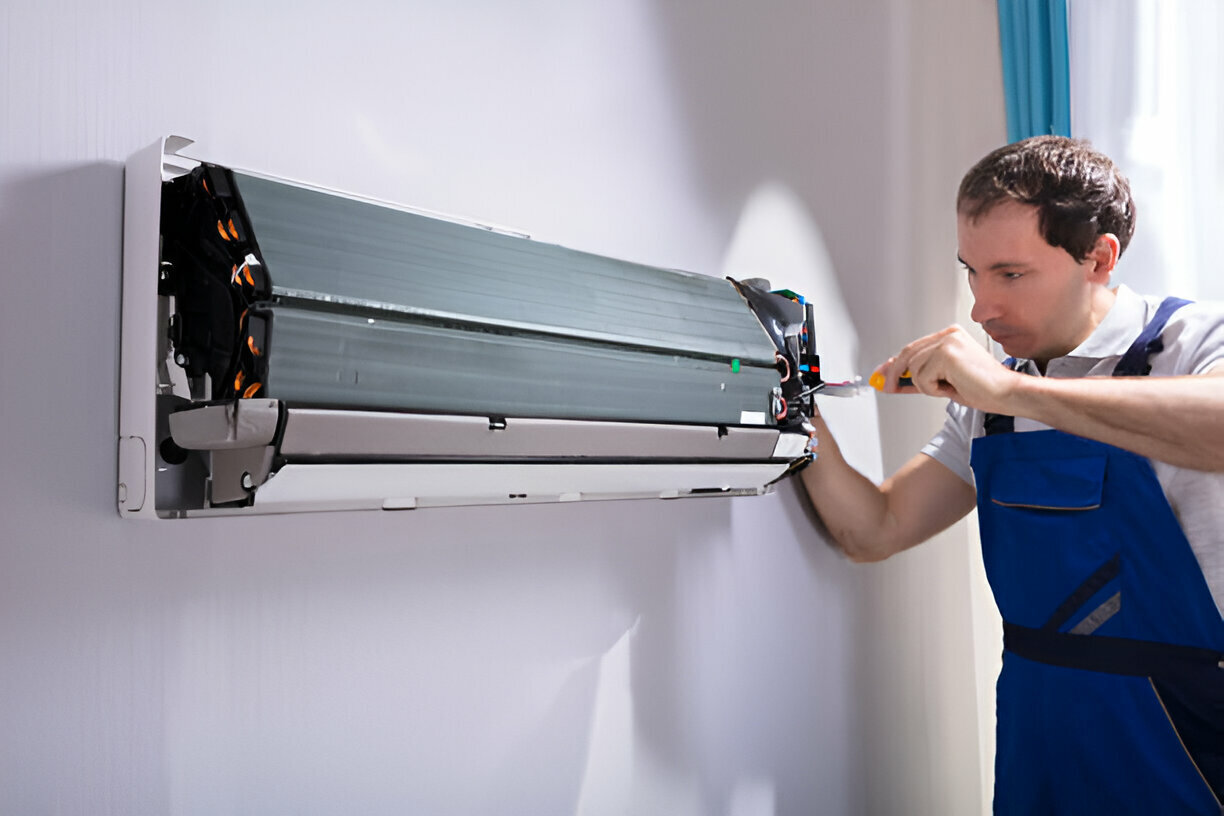 Technician repairing air conditioning unit with screwdriver on wall