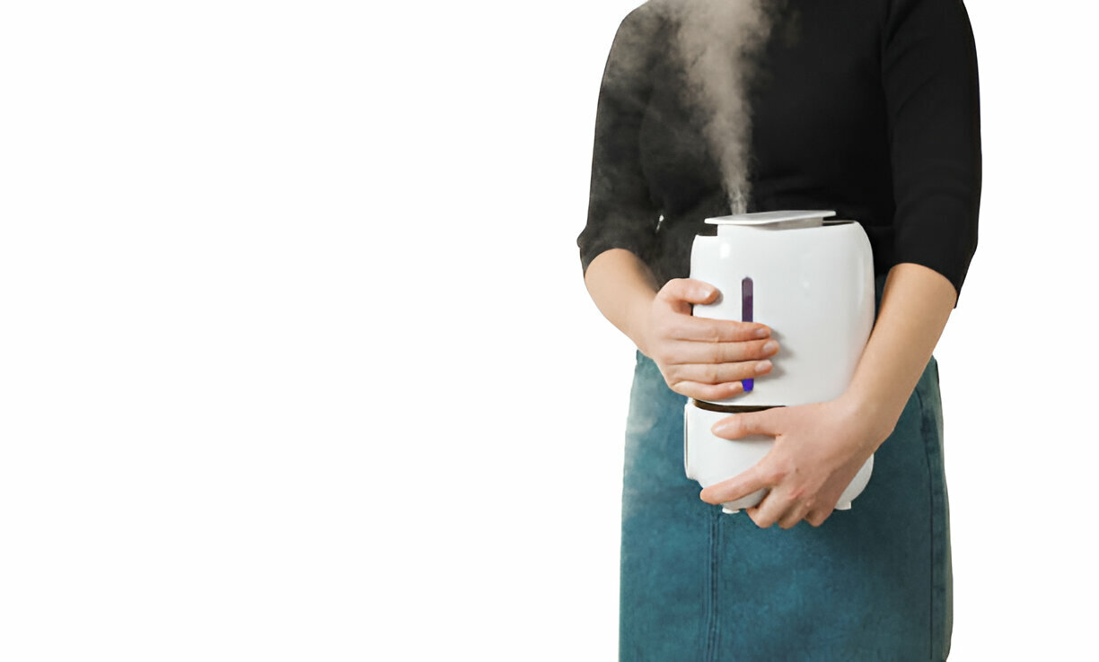 Person holding a white humidifier with steam rising, wearing teal skirt