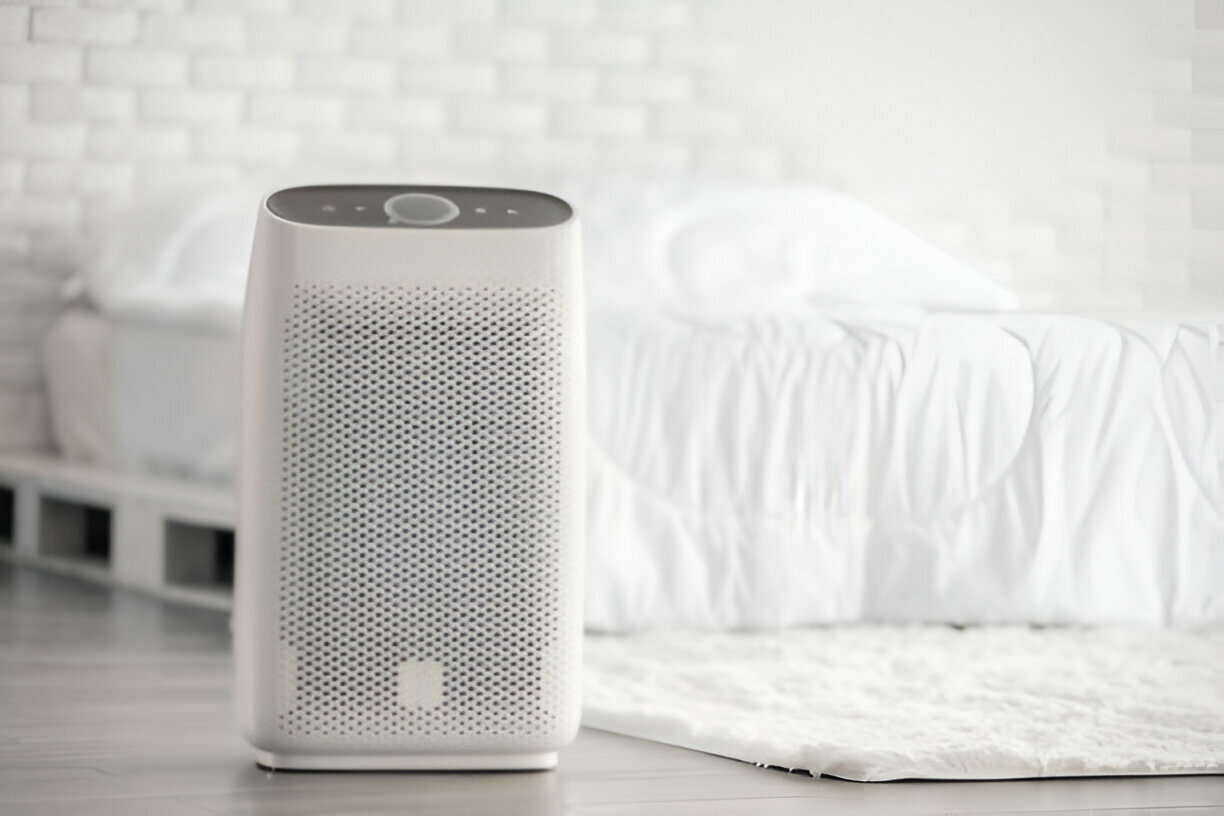 White air purifier on floor near bed in minimalist bedroom setting