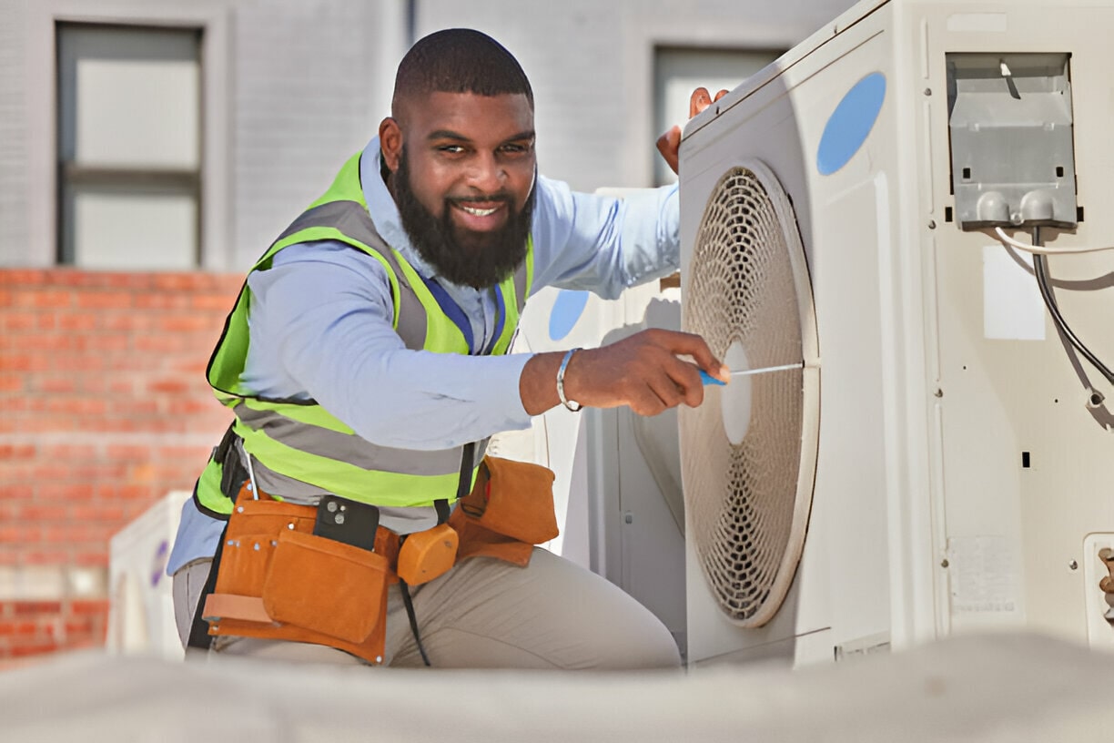 Technician in safety vest repairs air conditioning unit outdoors
