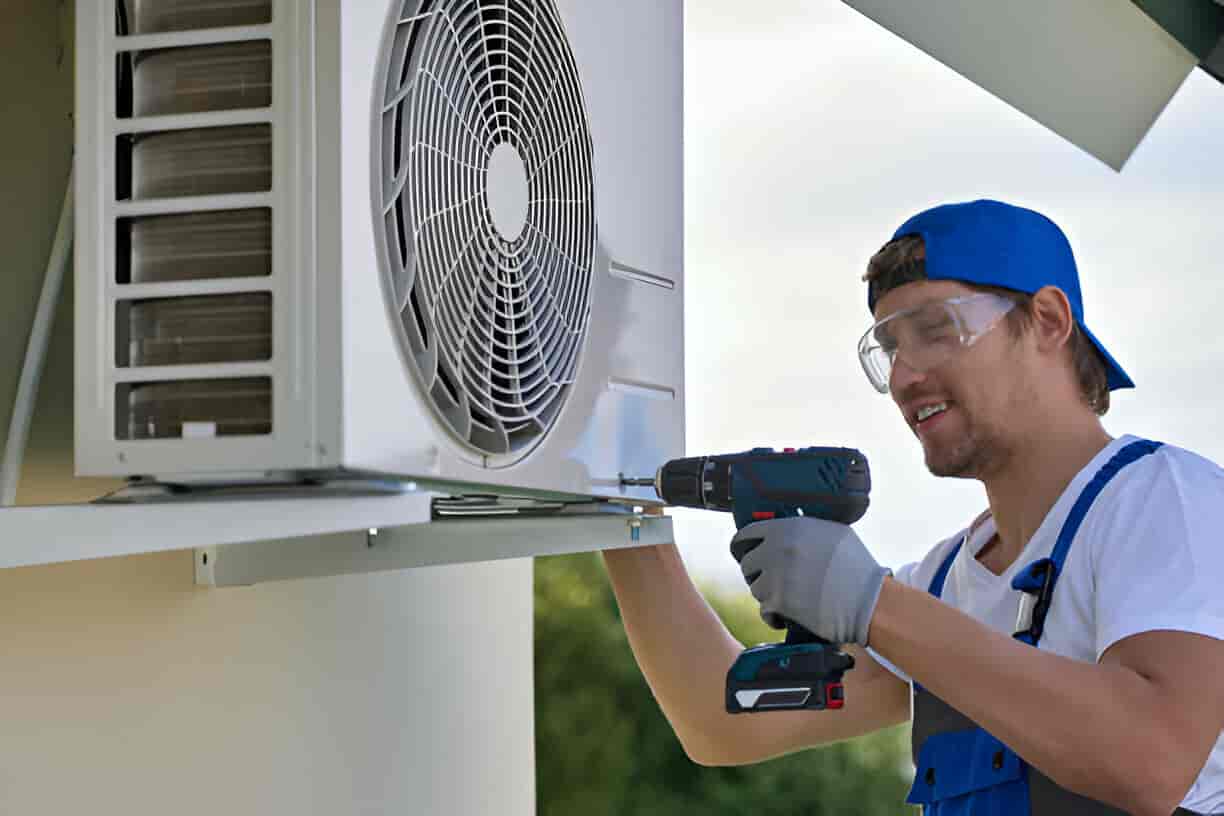 Technician installing air conditioning unit with drill and protective gear