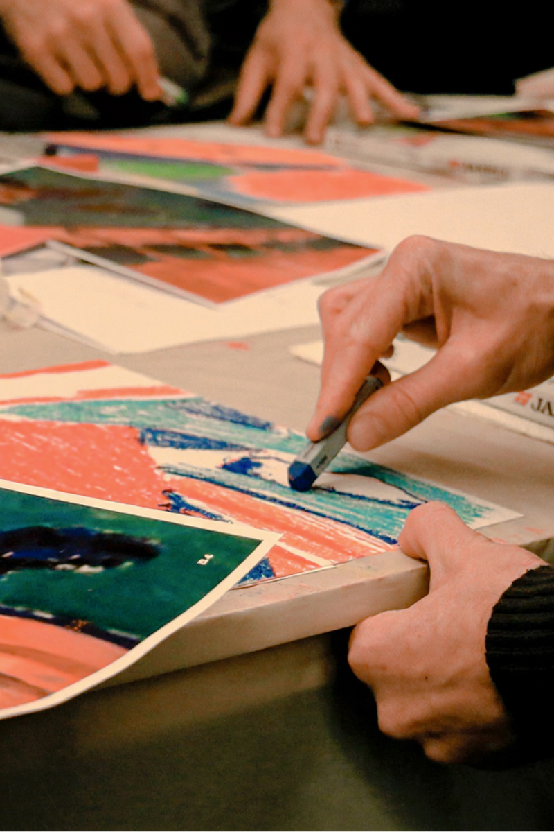 Main dessinant au pastel coloré sur une grand table un détail de la fresque pendant un team building fresque