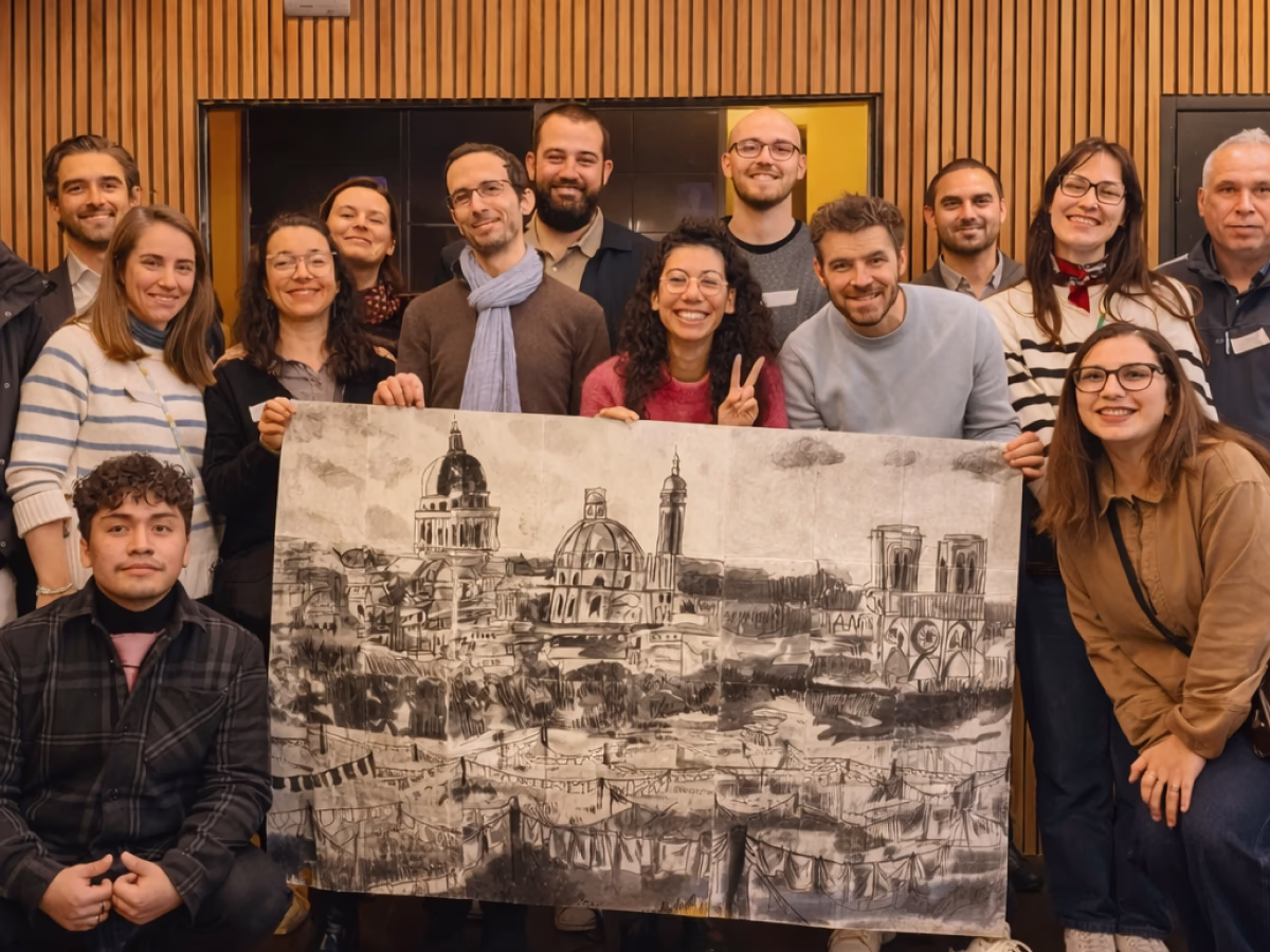 Une équipe pose devant la fresque qu'ils ont réalisé. La fresque est une composition de l'ensemble de dessin de chacun des membre de l'équipe qui finit pas représenté une architecture au fusain