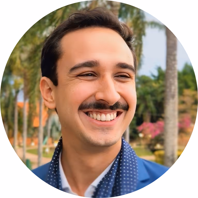 Smiling man with mustache in blue jacket, round portrait with outdoor background.
