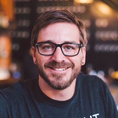 Smiling man with glasses in a warm indoor setting.