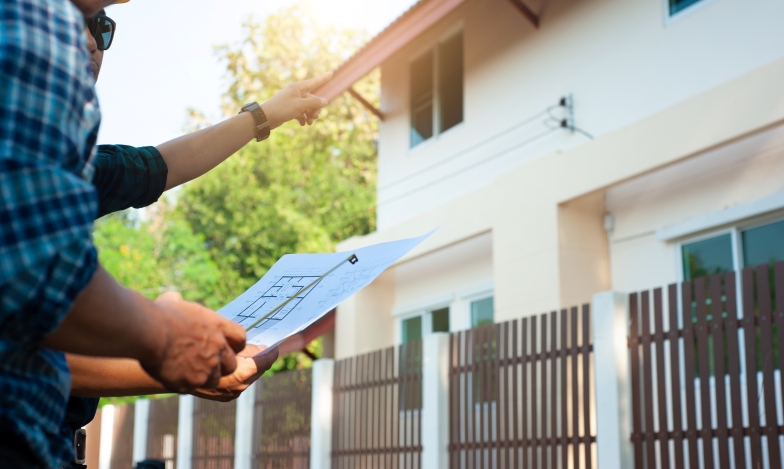 Two men examining a house exterior plan and pointing at the roof under sunny daylight. Showcasing appraisal reviews.