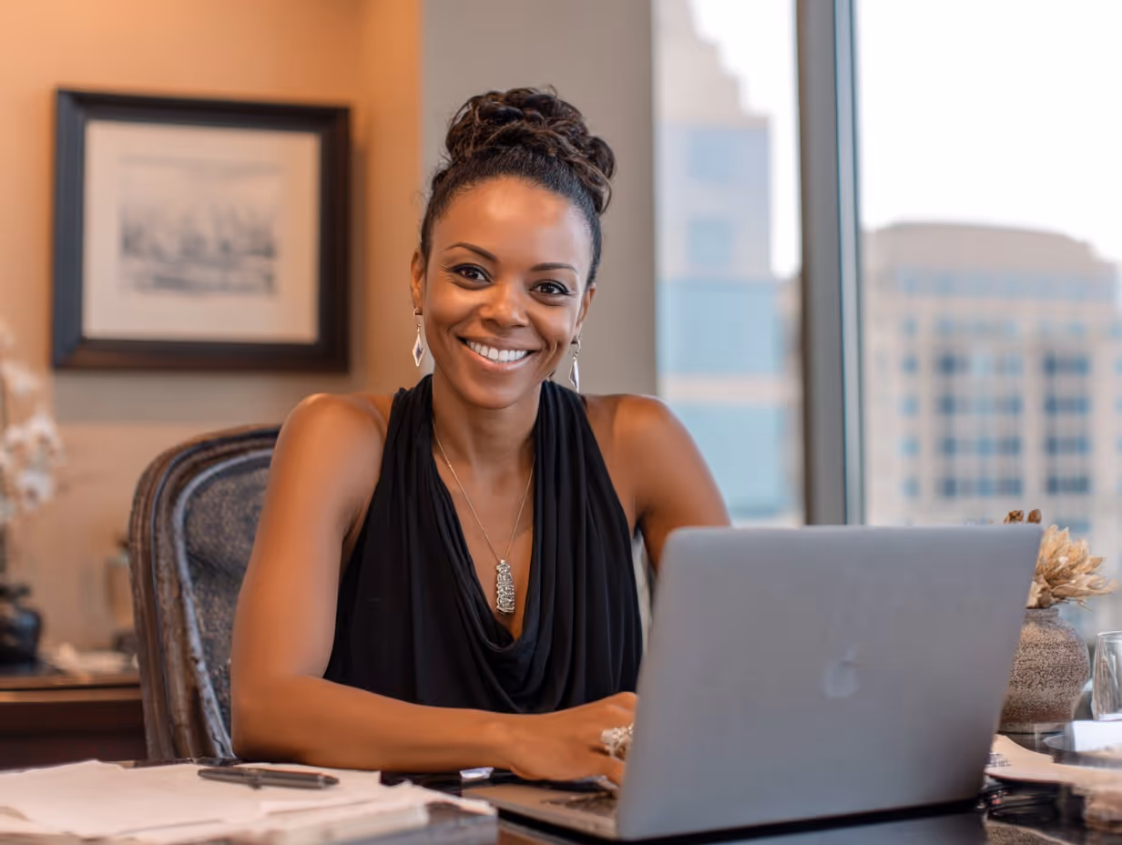 Photo of a smiling, professional woman working at a laptop in a modern office, symbolizing real estate expertise, virtual consulting, and seamless online financial planning.
