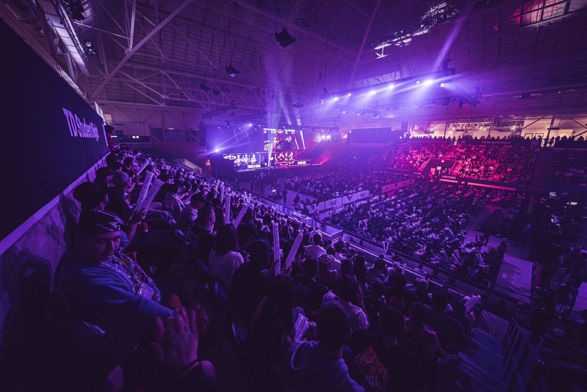 Large crowd watching an esports or gaming event in an indoor arena with purple and pink lighting.